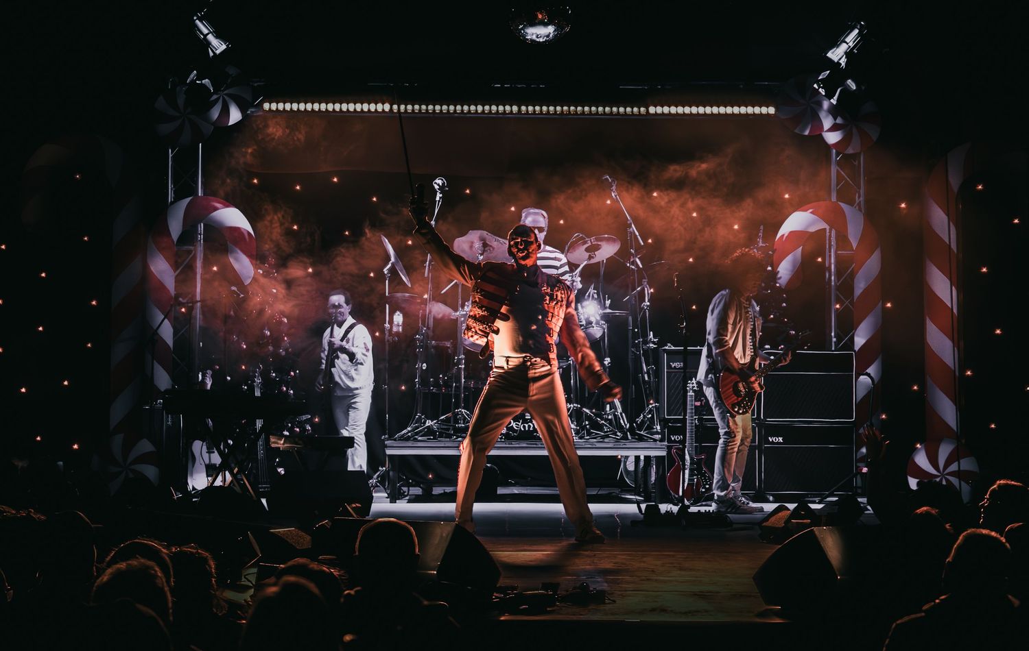Concert stage performance with dramatic lighting and musicians performing live for an energetic crowd.