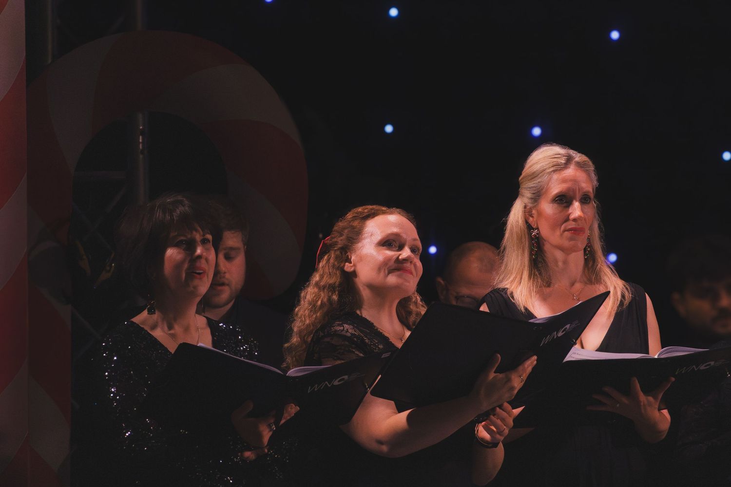 Vocalists in formal black attire performing during an evening concert.