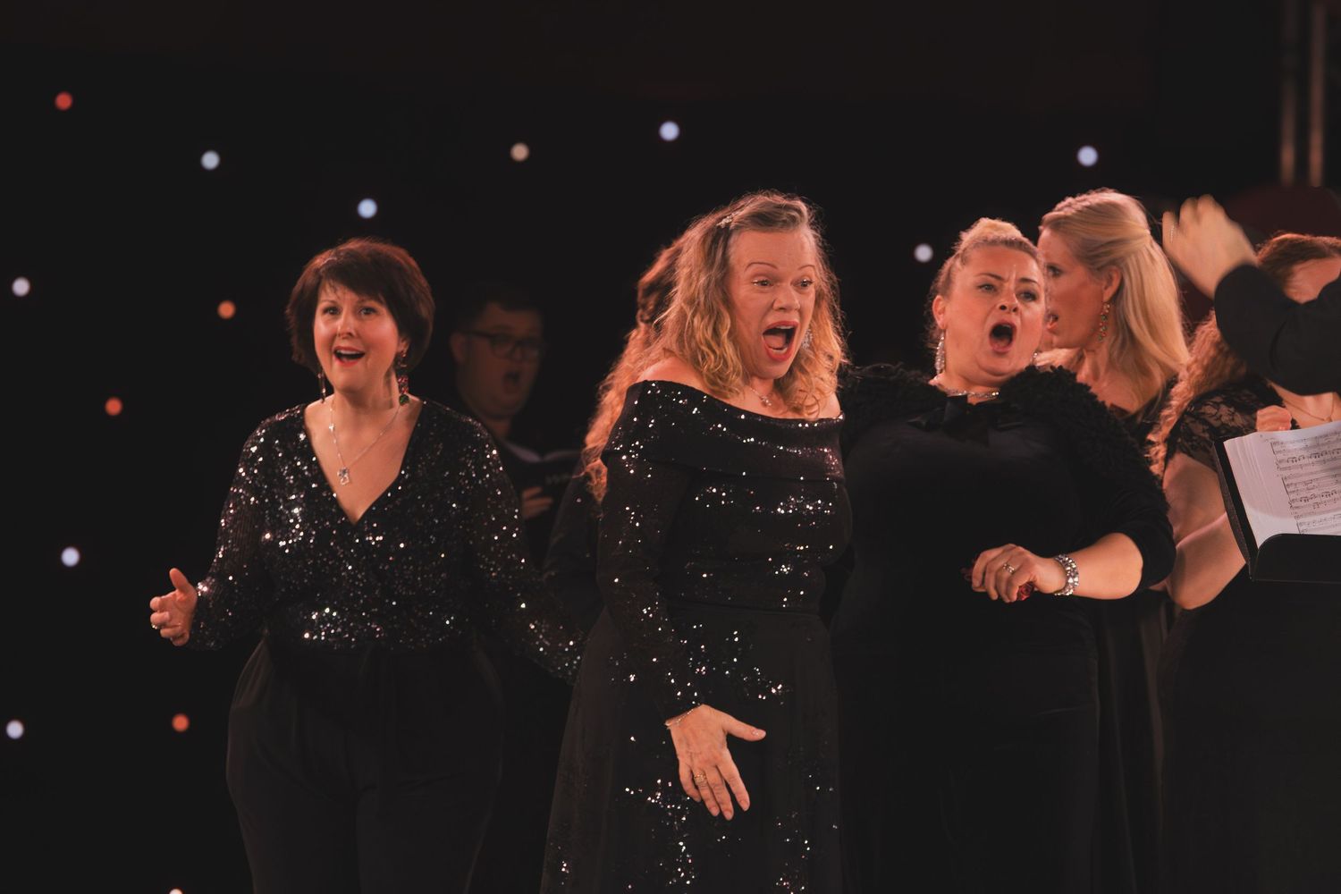 Choir members in sparkly outfits performing during an evening concert.