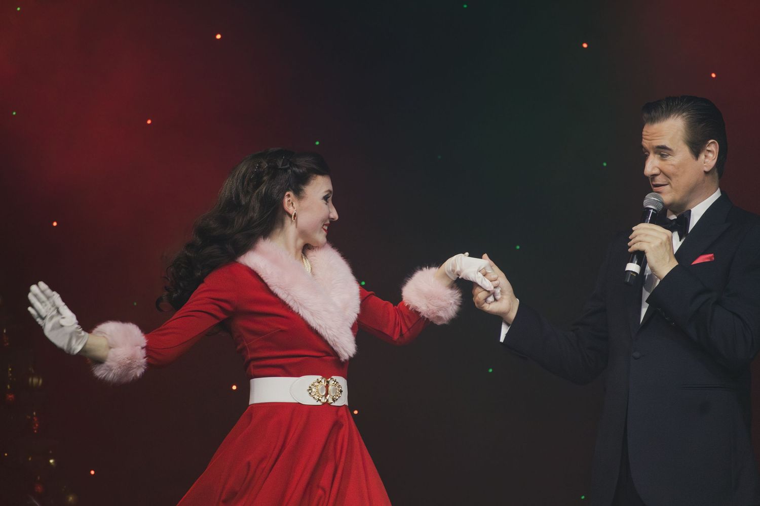 Performers dancing together during an elegant stage show with dramatic lighting.