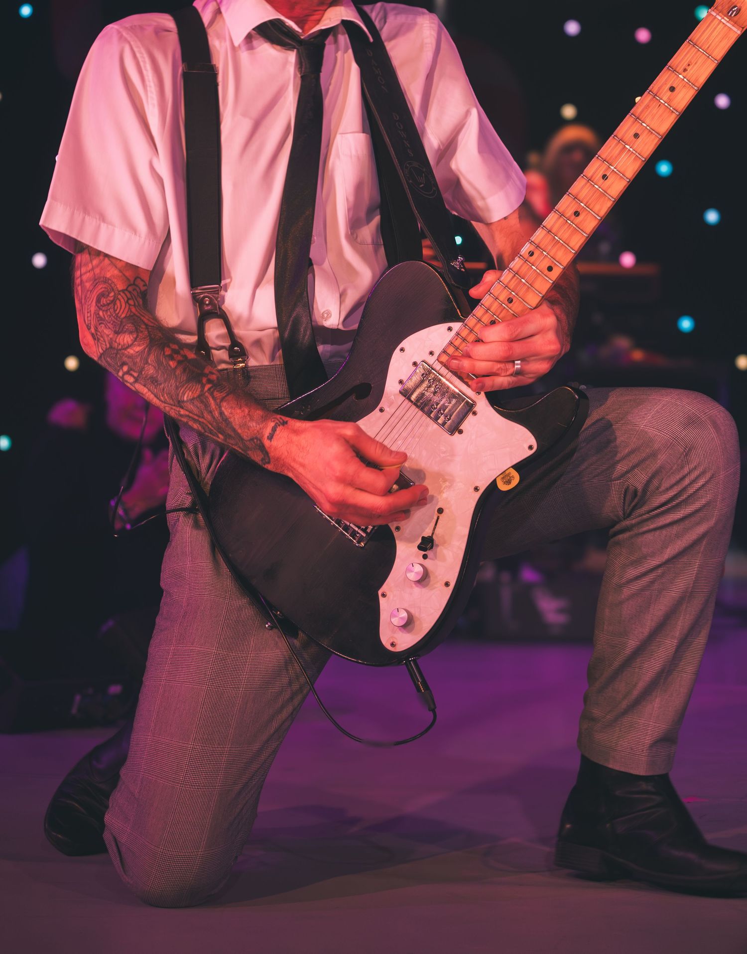 Close-up of a guitarist in suspenders playing a pink electric guitar on stage.