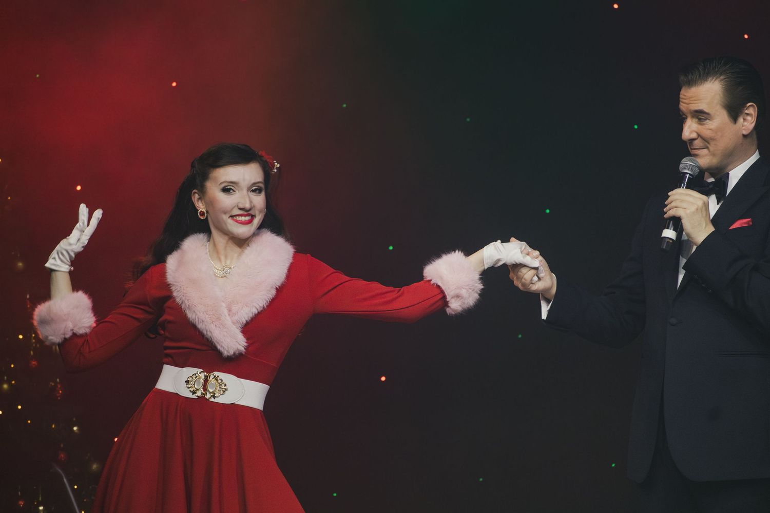Elegant holiday stage show with performers in formal attire and festive costumes.