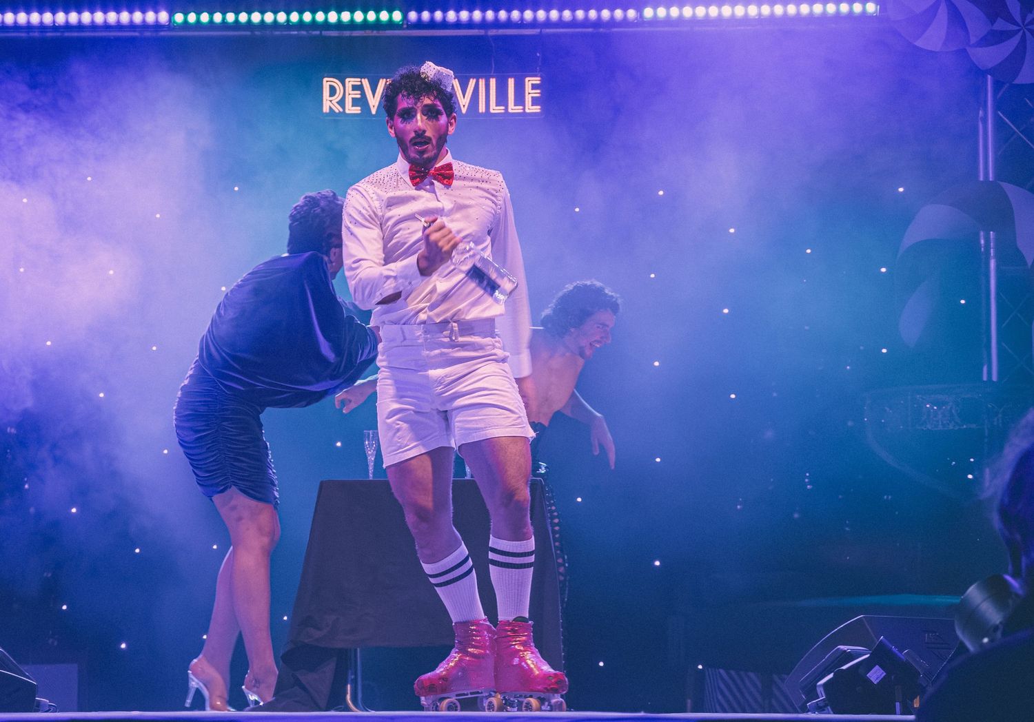 Stage performers in white costumes dance under blue theatrical lighting at a live show.