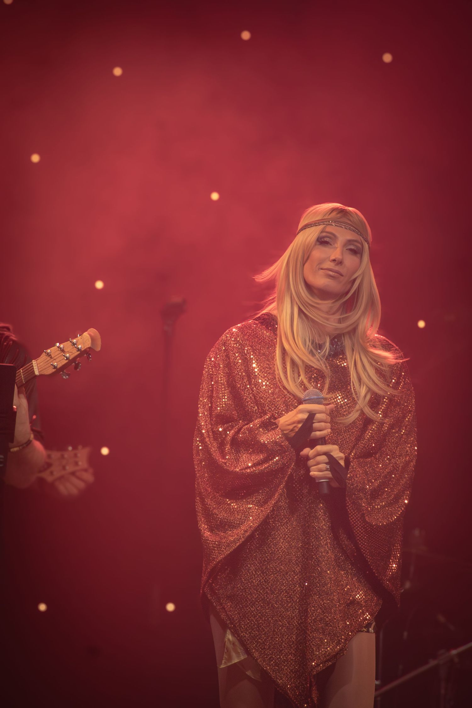 Singer in glittering dress performing under atmospheric red lighting with bokeh effects.