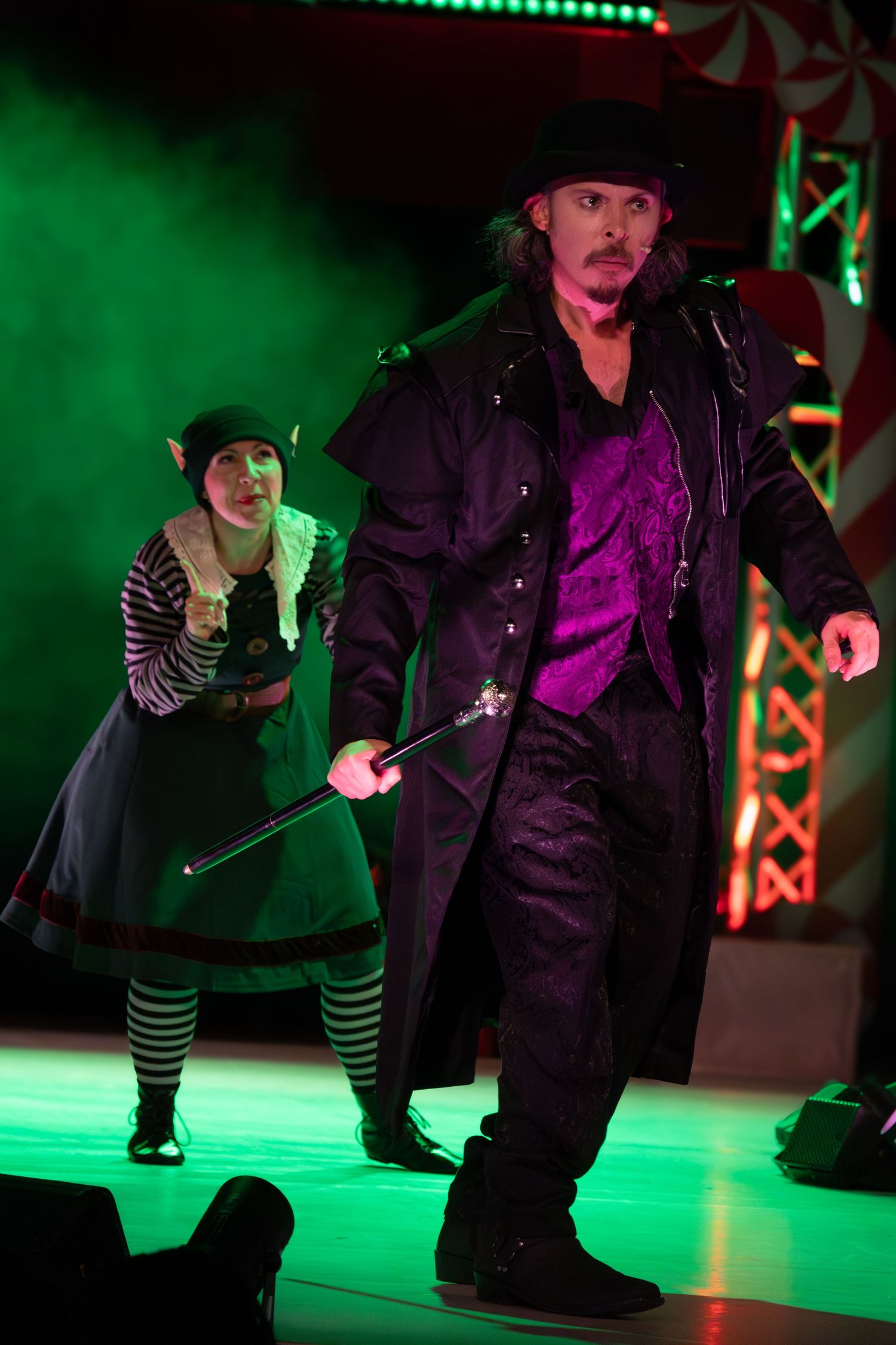 Theatrical scene with performers in dark costumes against green-lit backdrop.