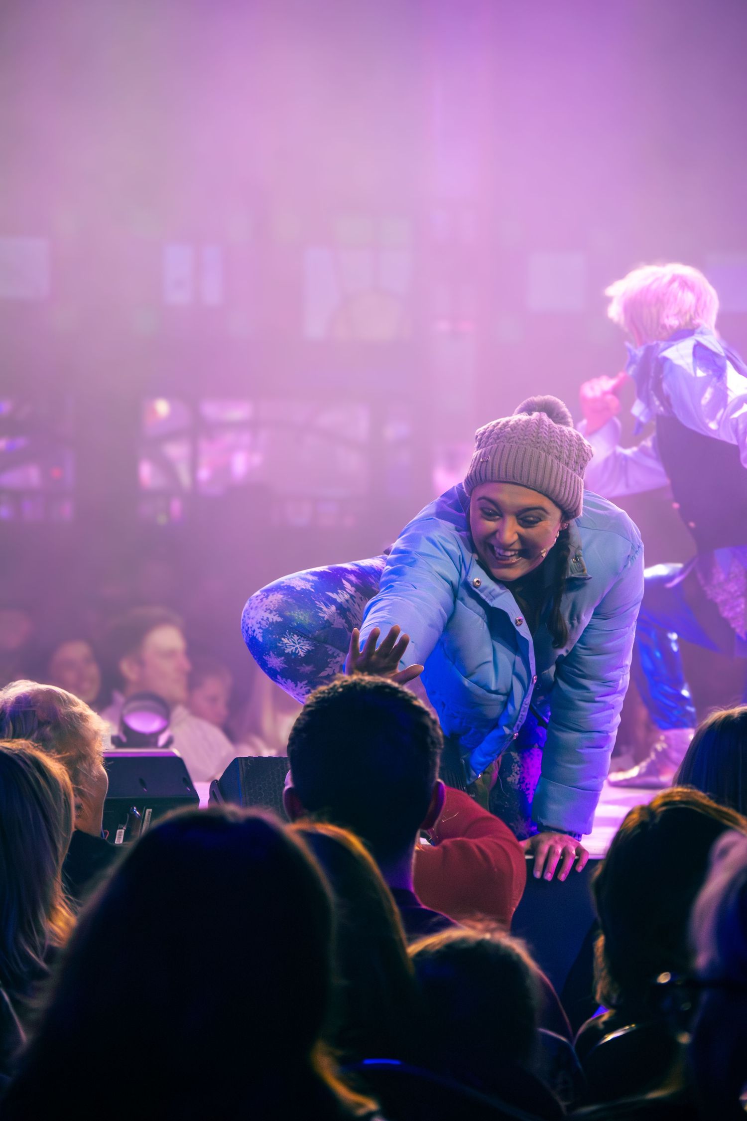 Performer interacts with audience members during a live show with purple stage lighting.