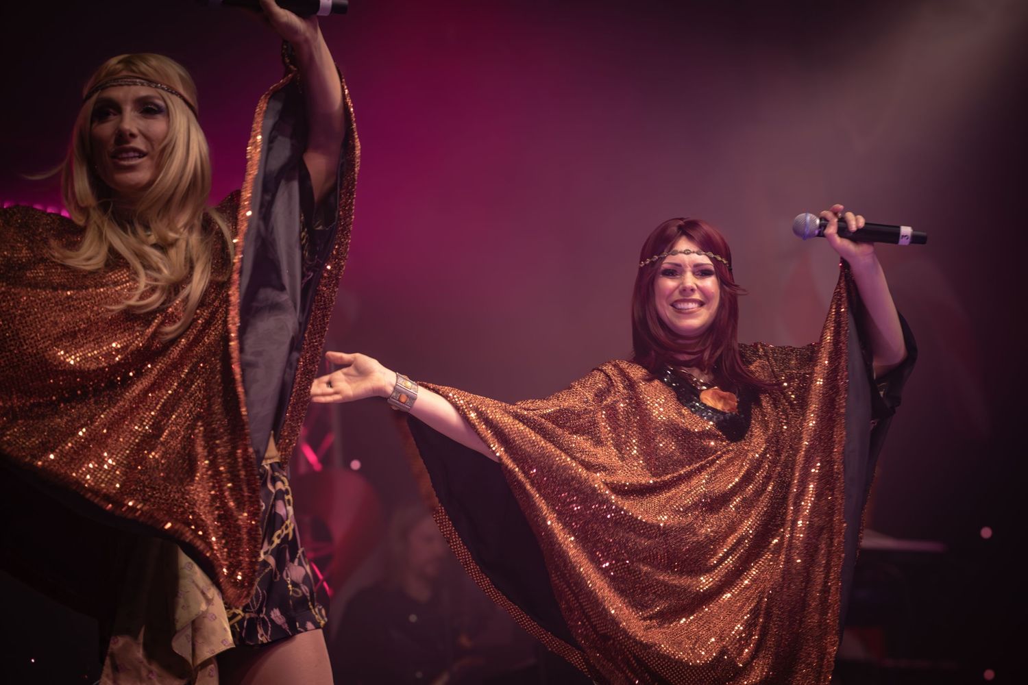 Performer in flowing metallic dress singing on stage with dramatic red lighting.