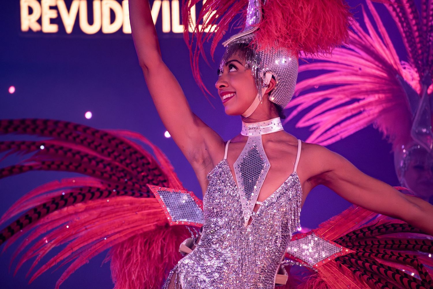 Revudeville stage show featuring performers in sparkling costumes under purple lighting.