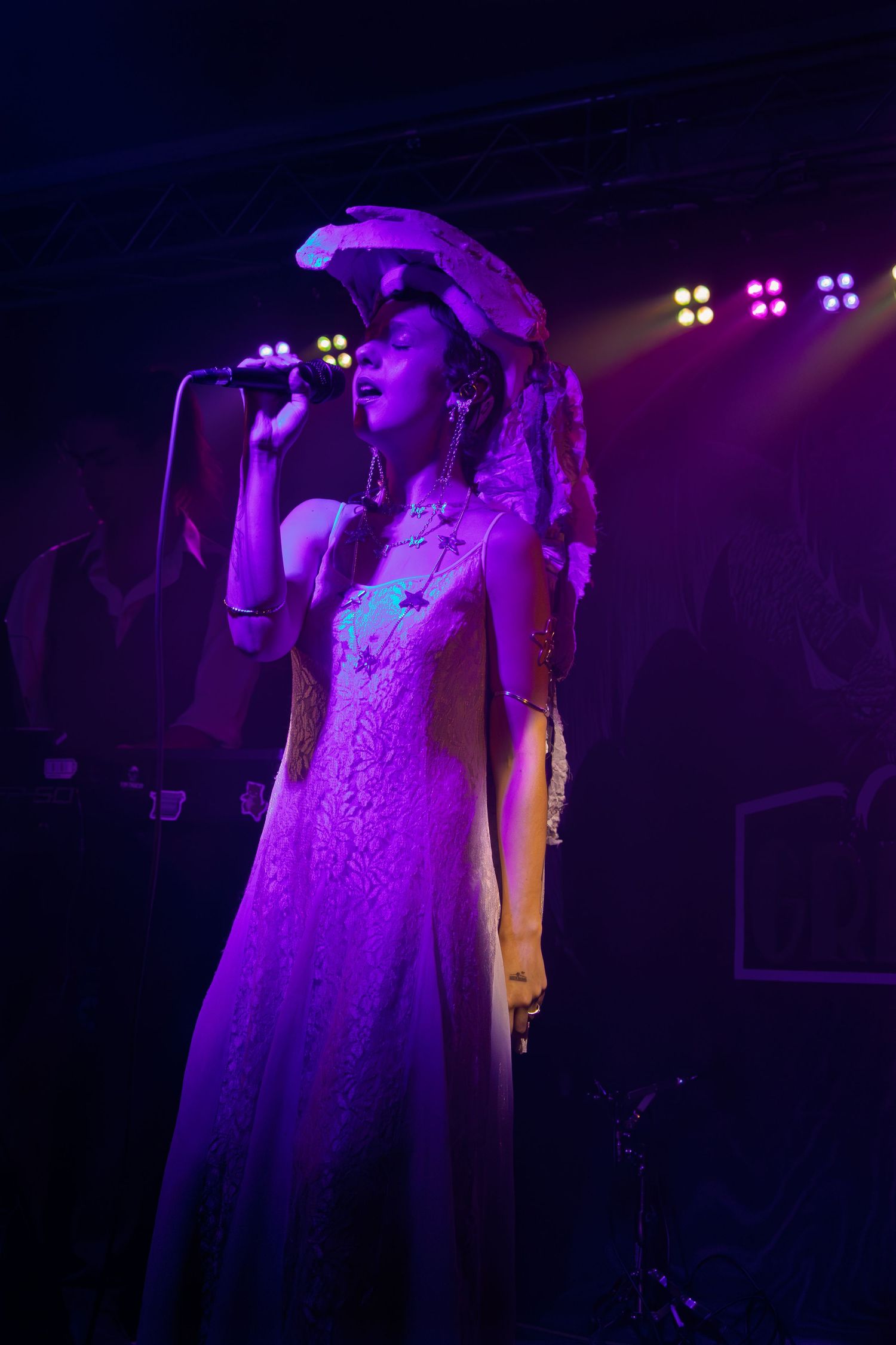 A white wedding dress illuminated by purple stage lighting creates a dramatic silhouette on a dark stage.