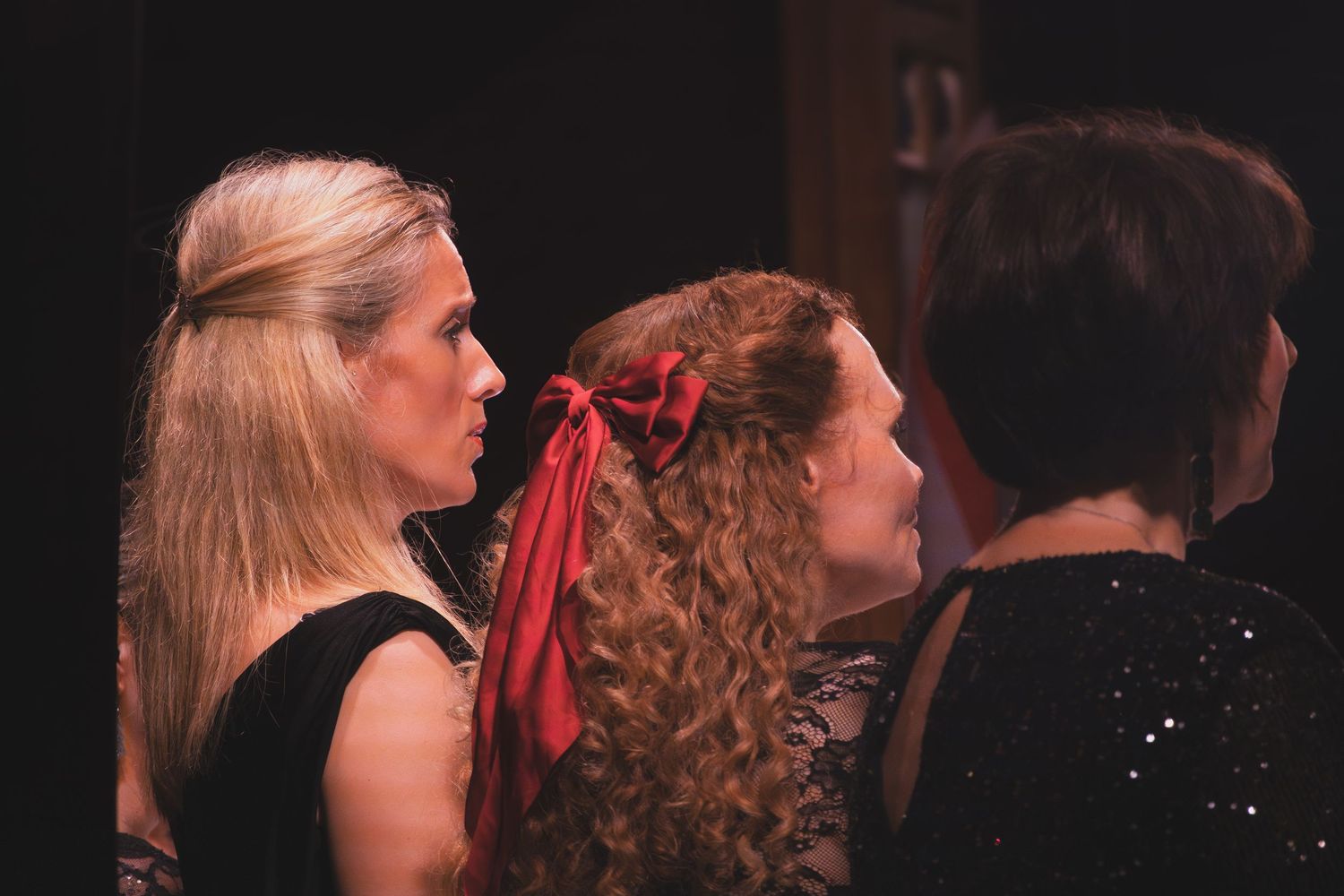 Performers in dark attire stand together on stage during a theatrical production.