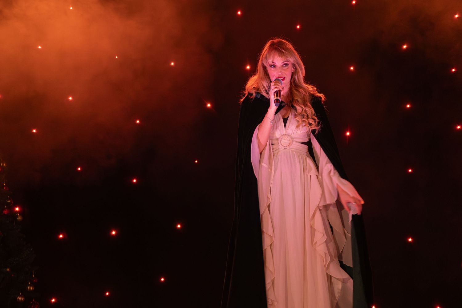 A stage performance featuring a flowing dress silhouette against red stage lighting and twinkling lights.