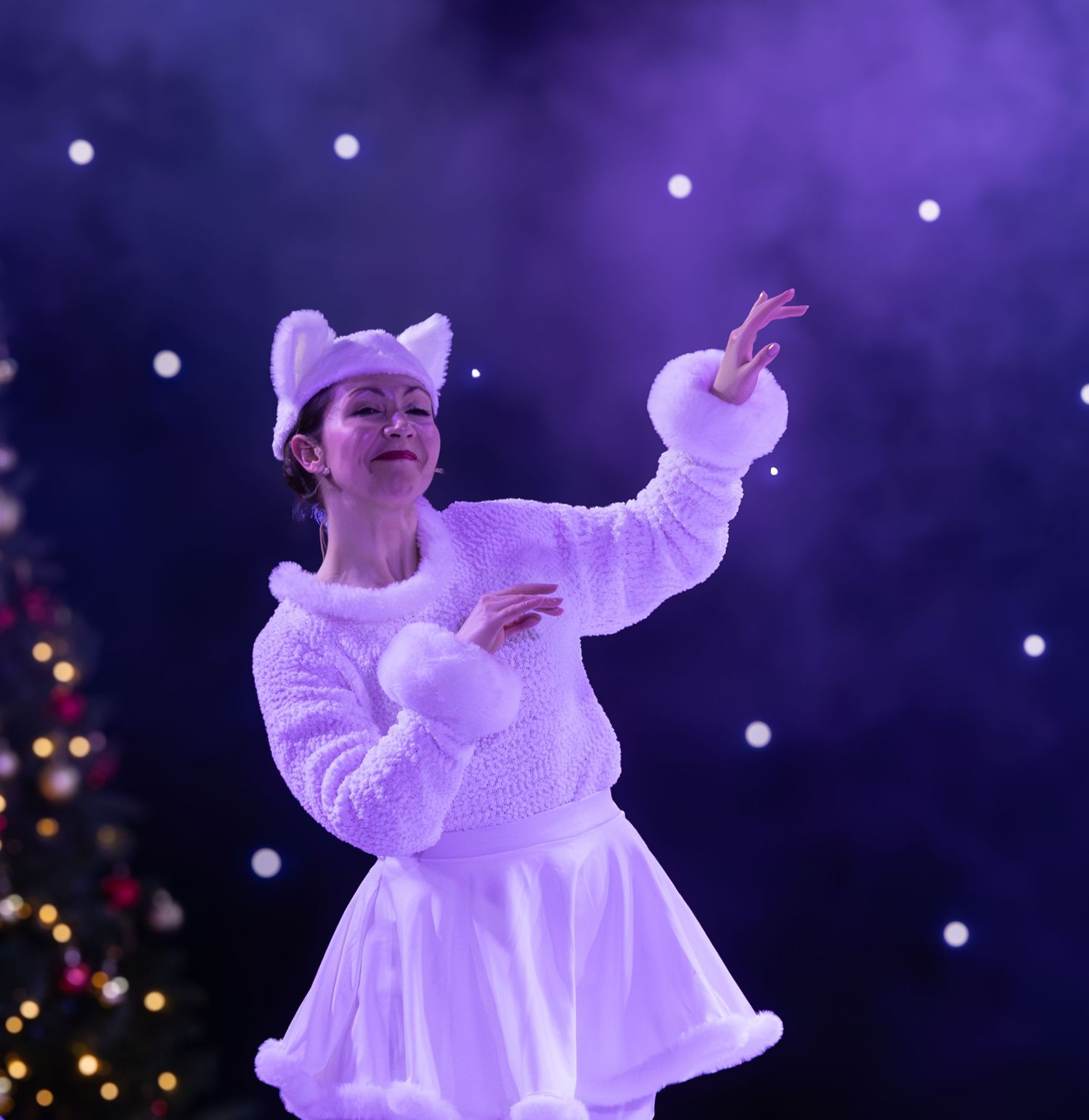 Dancers in flowing white costumes perform against a purple starlit backdrop.