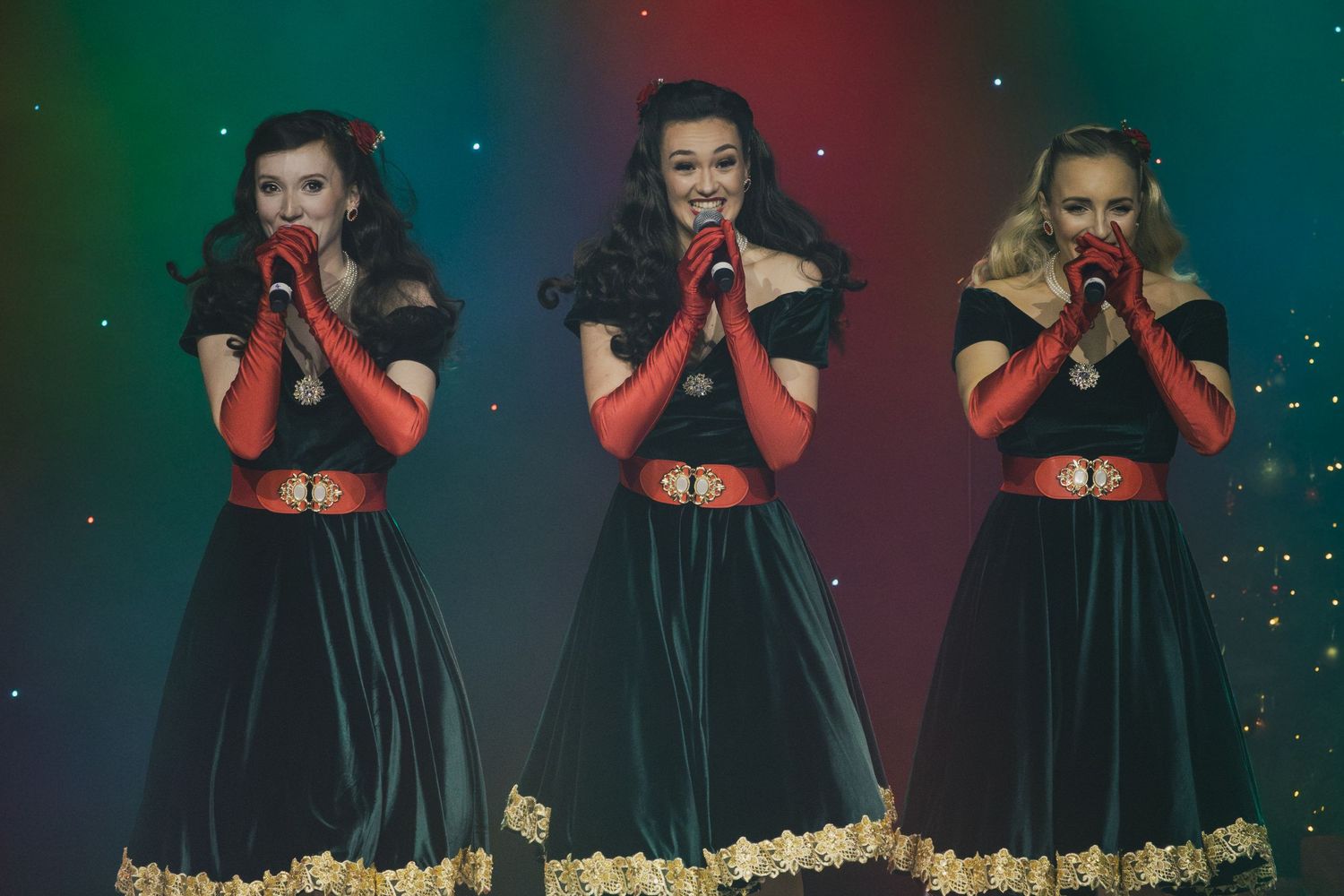 Three performers in matching black and red dresses perform choreographed moves on stage.