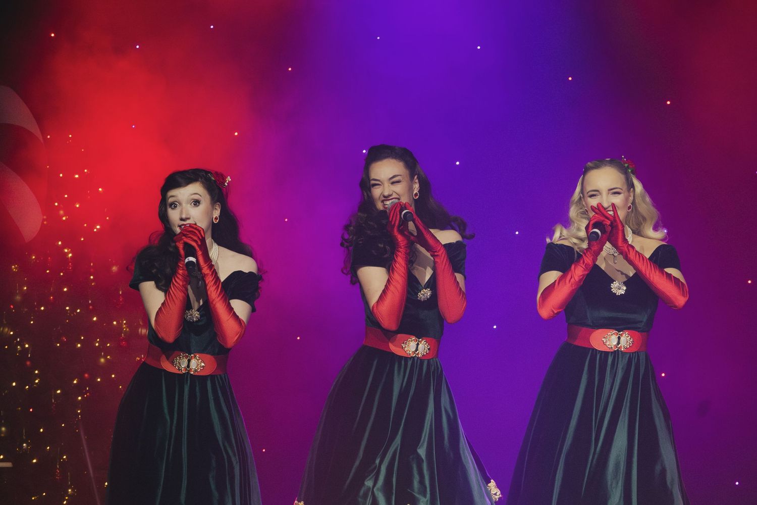 Three performers in matching outfits dance synchronously under vibrant red and purple lighting.