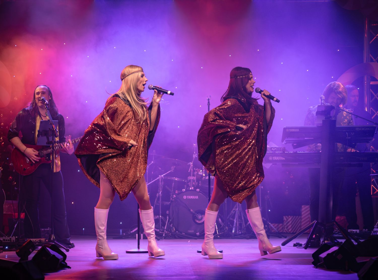 Performers in sequined outfits execute synchronized dance moves on illuminated stage.