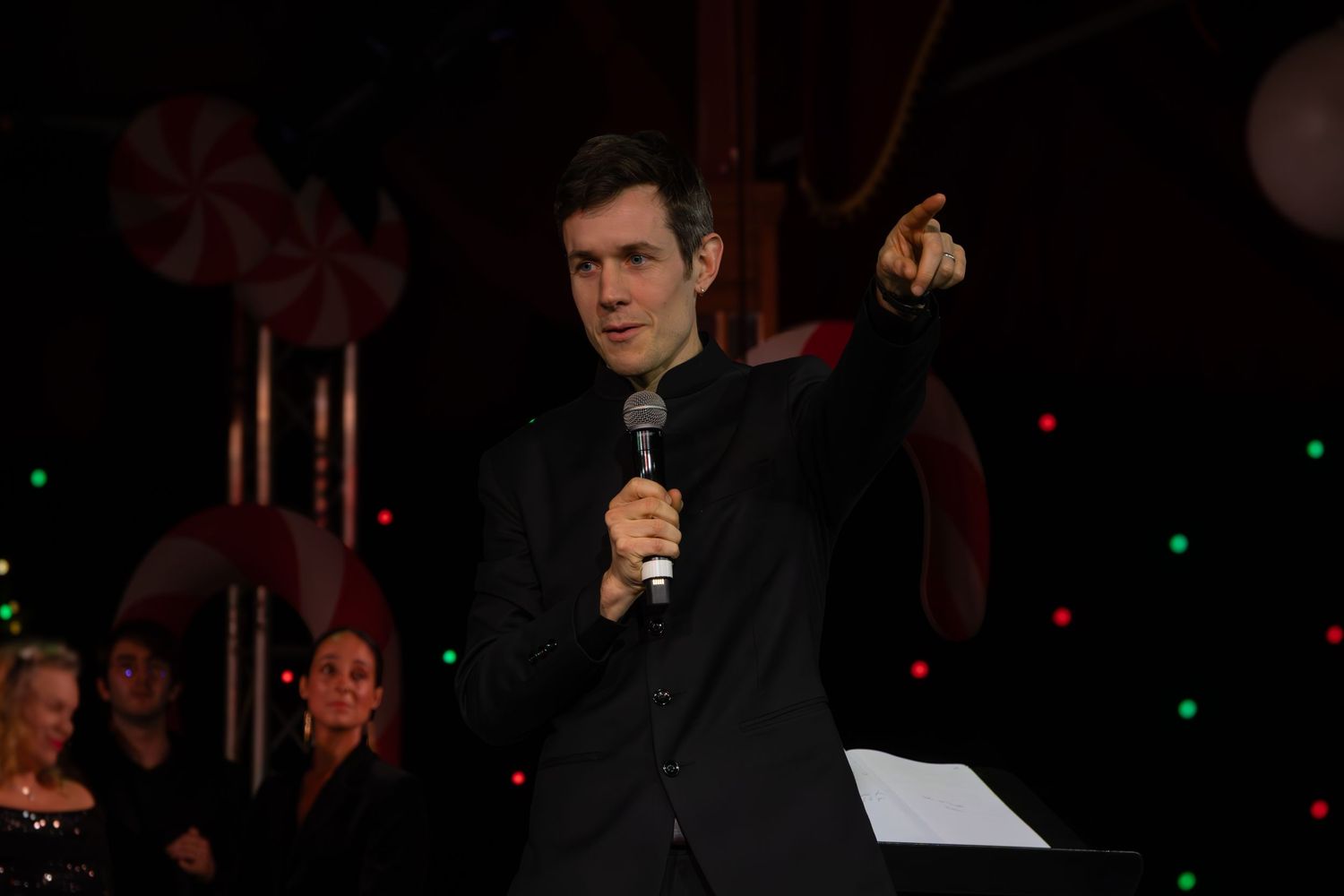 Performers in black formal wear sing during a darkened stage performance.