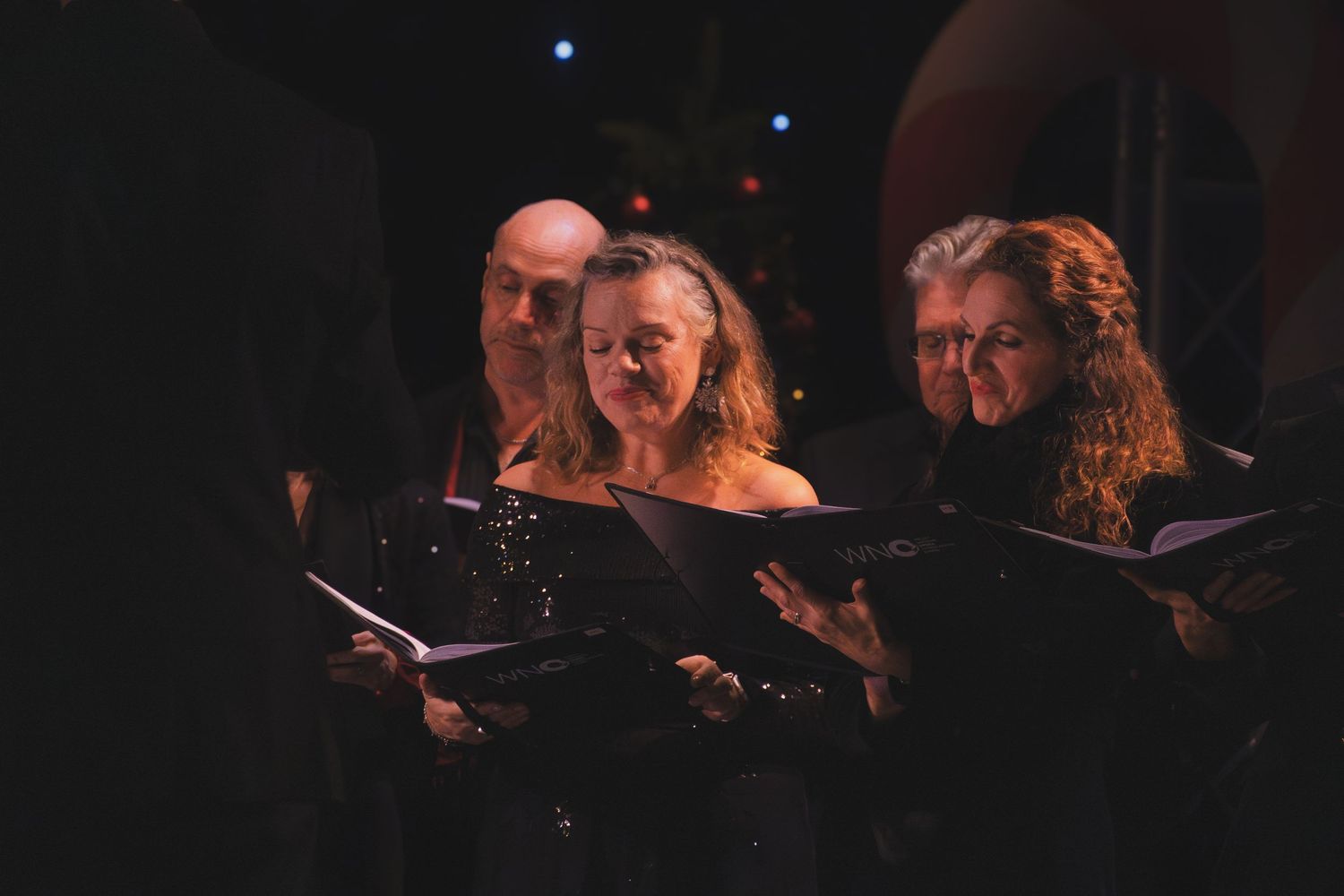 Choral singers perform in a darkened concert hall with blue stage lighting.
