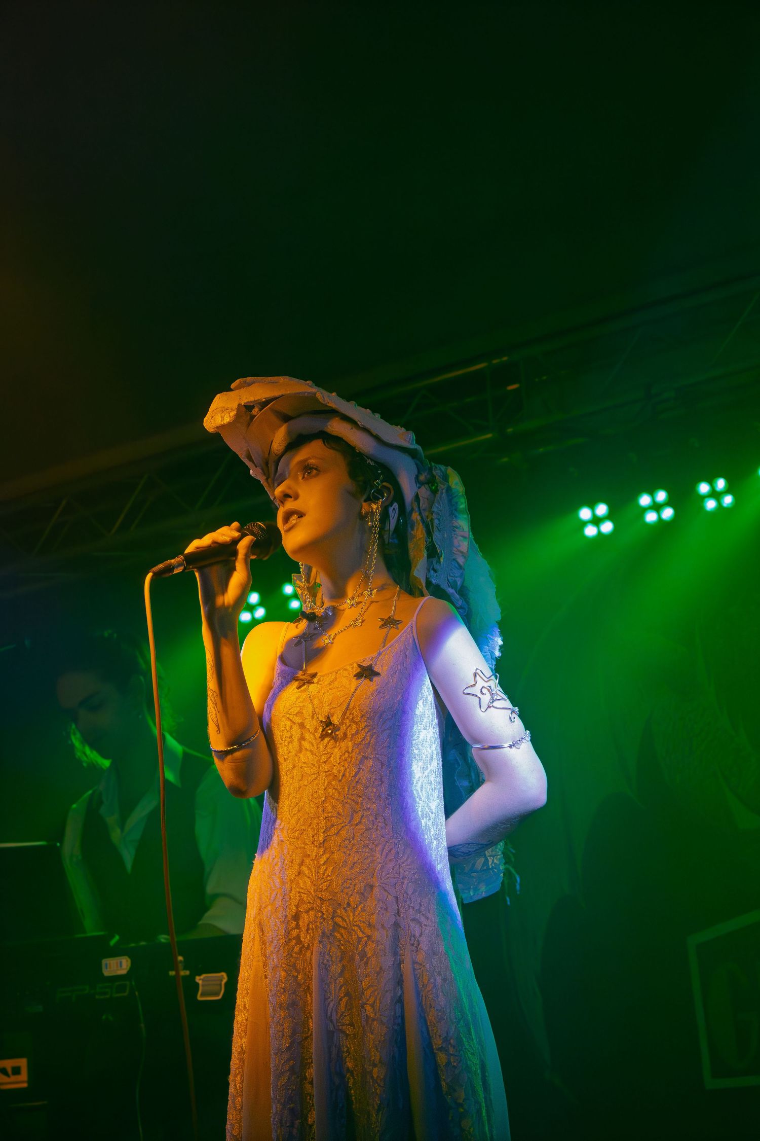 A performer in a white dress sings on stage under dramatic green lighting at a concert venue.