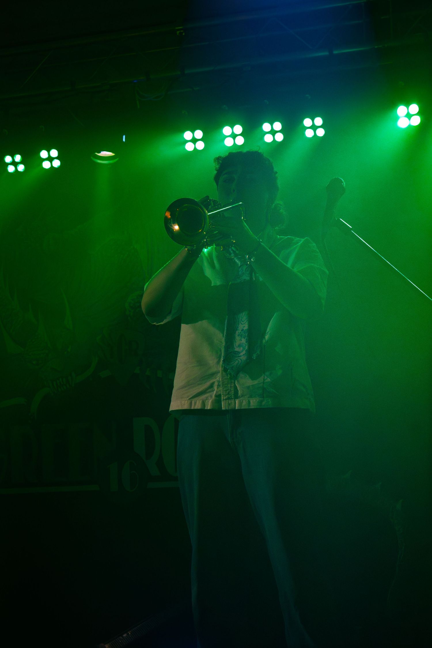 Silhouetted figures performing on stage with bright green spotlights and atmospheric effects.