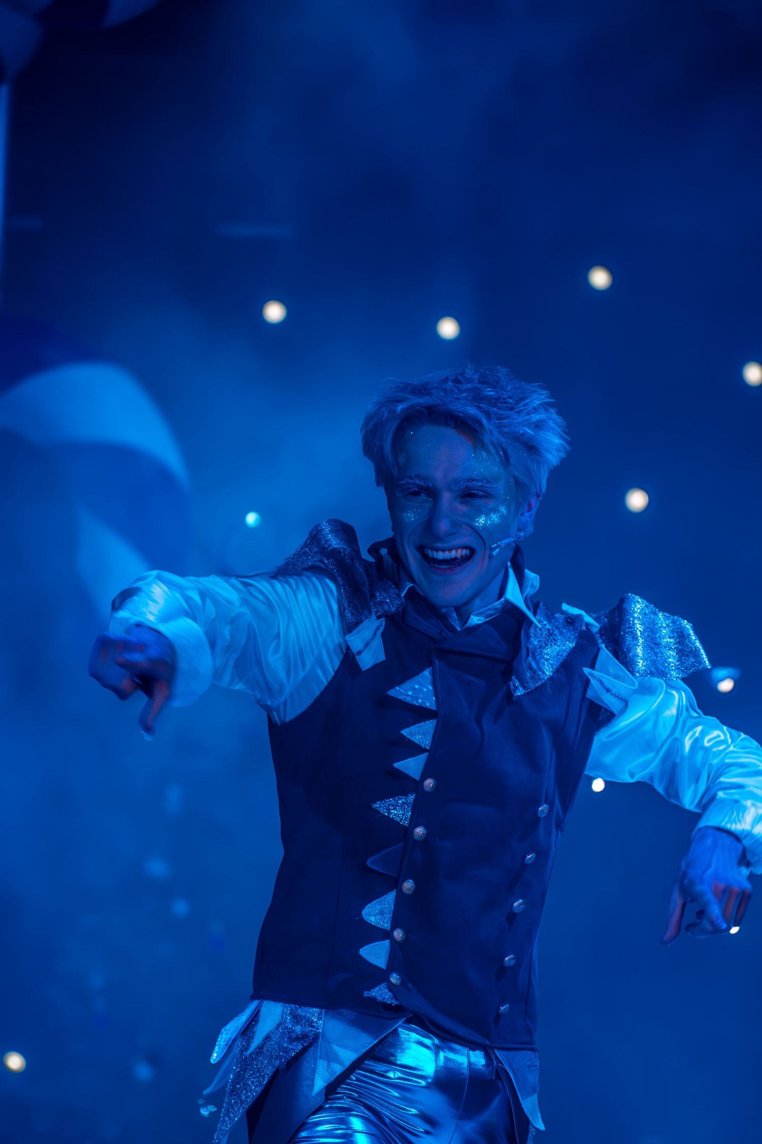 Performer in period costume moves expressively on stage with blue lighting effects.