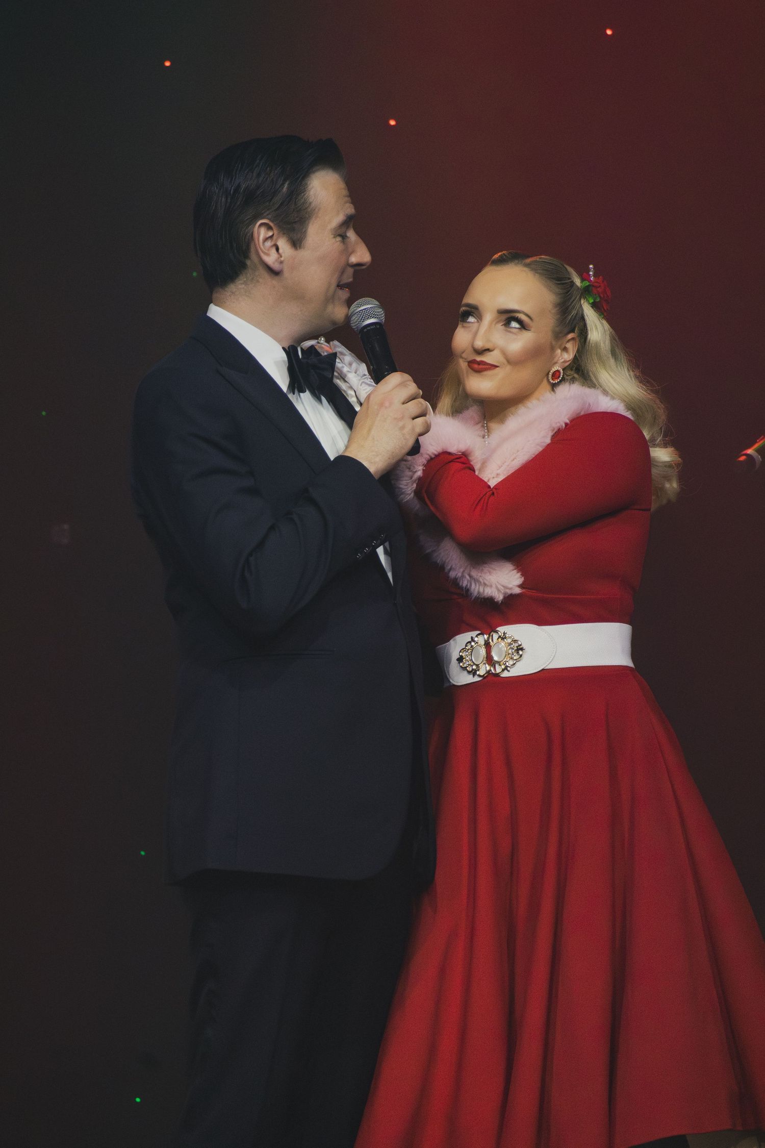 A couple performs a romantic dance scene in formal attire with the woman wearing a striking red dress.