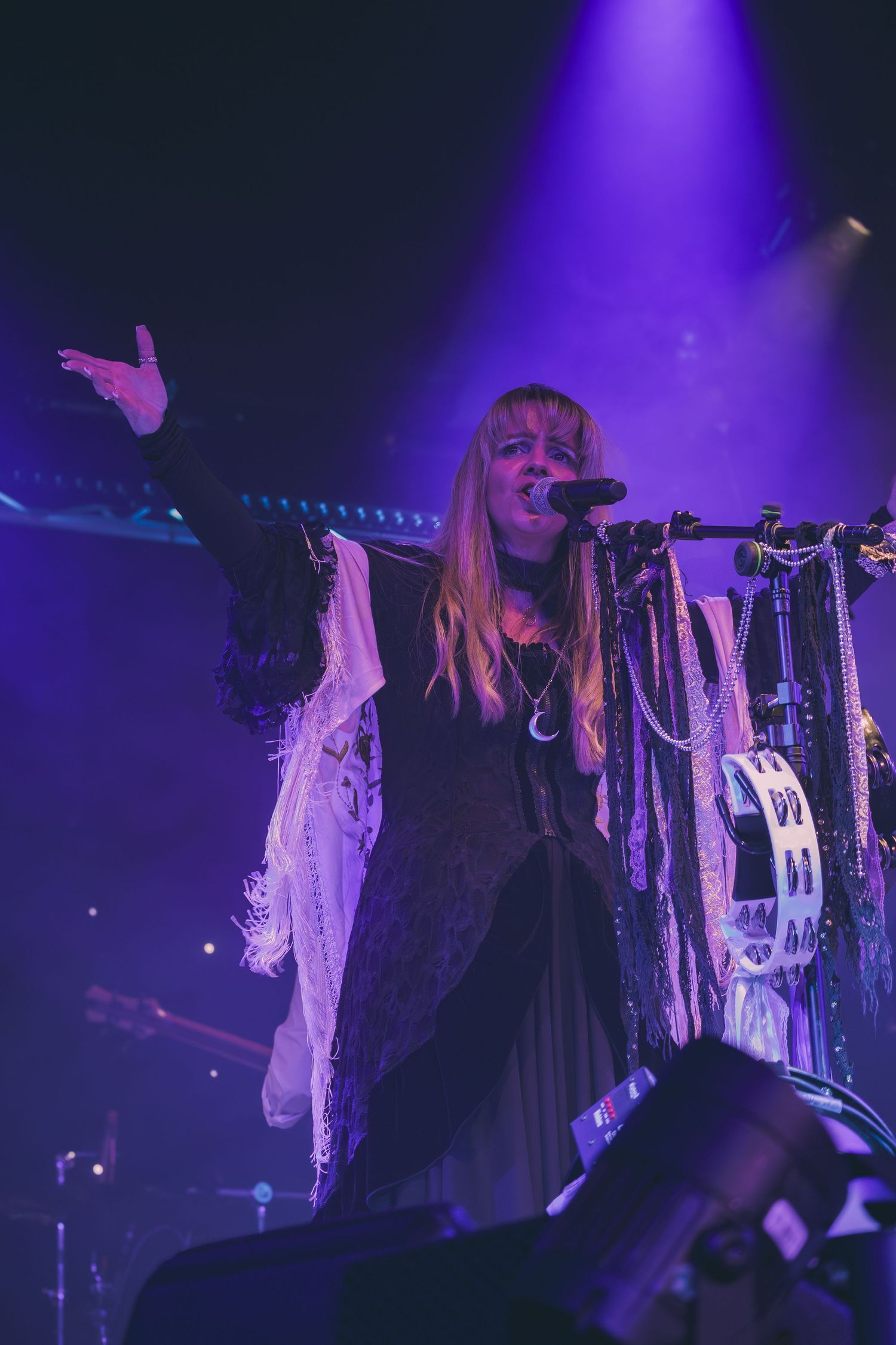 Concert performer in dark attire illuminated by dramatic purple stage lighting.