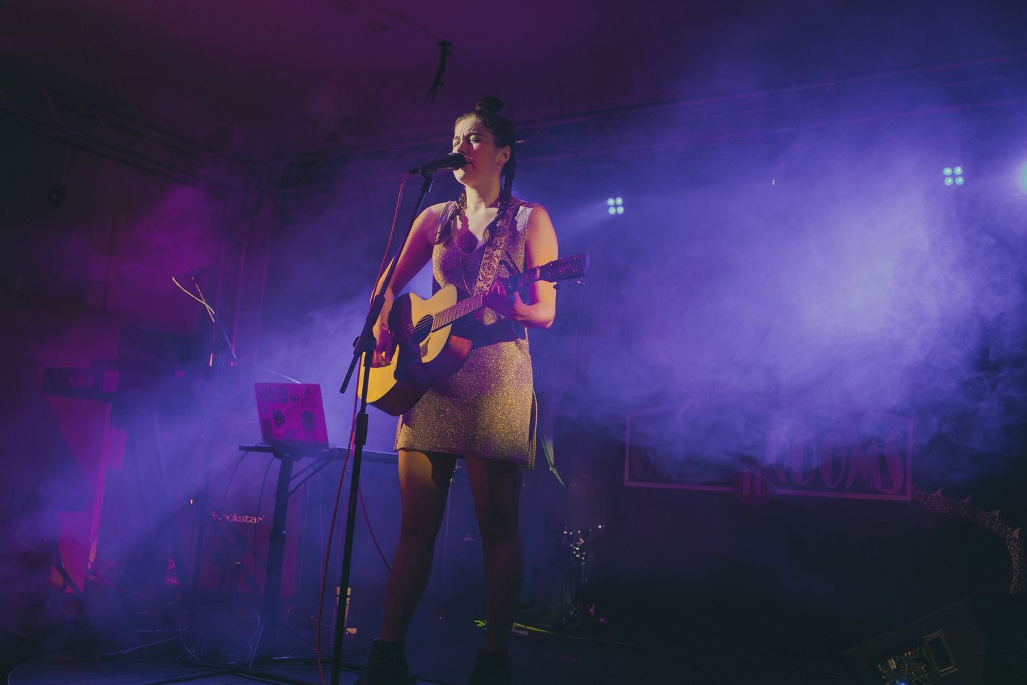 A performer sings passionately on stage surrounded by dramatic purple and blue lighting effects during a concert.