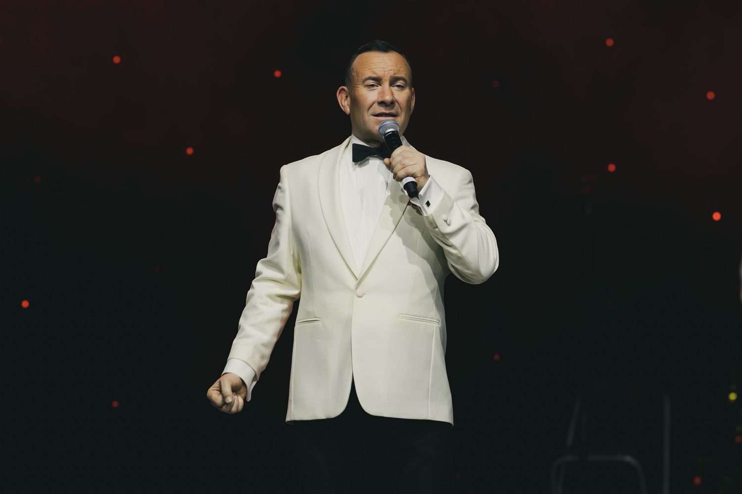 Performer in white jacket sings emotively on dimly lit stage.