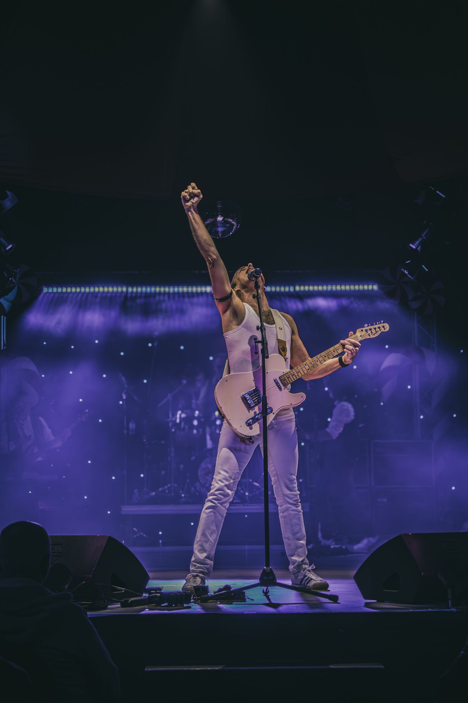Musicians performing on stage with purple and blue lighting creating a dramatic concert atmosphere.