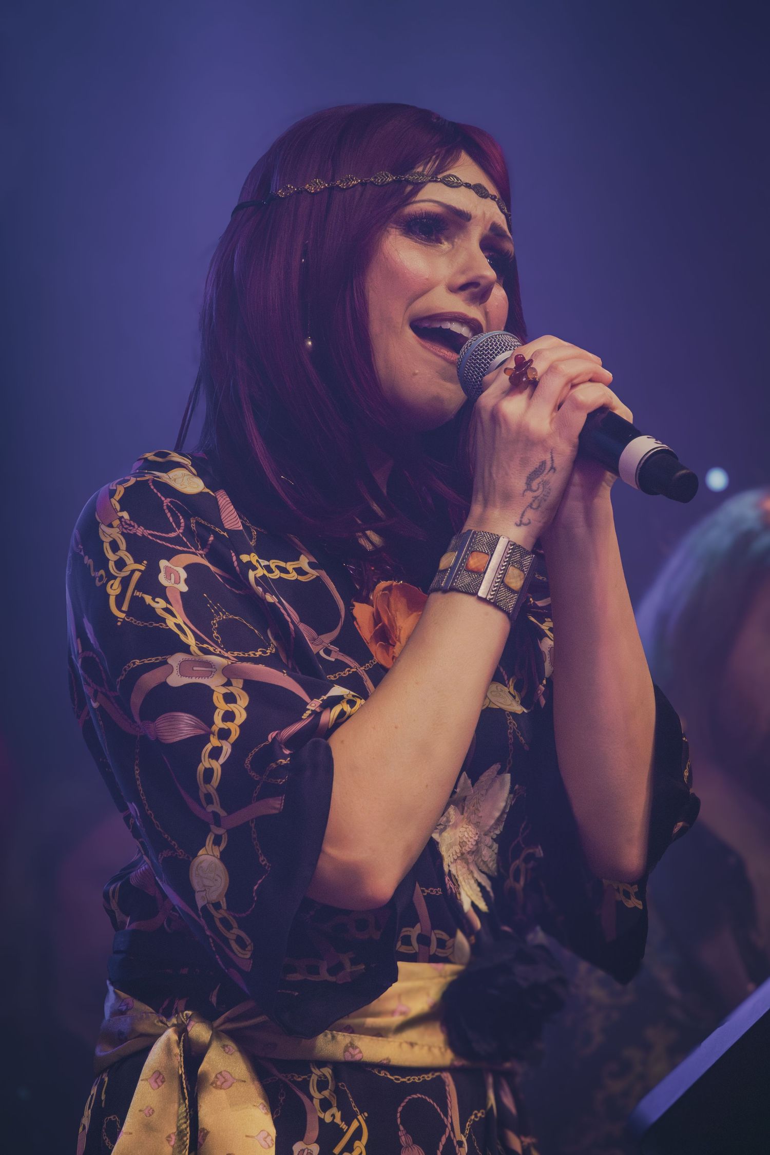 Performer singing into microphone wearing patterned outfit under blue stage lights.