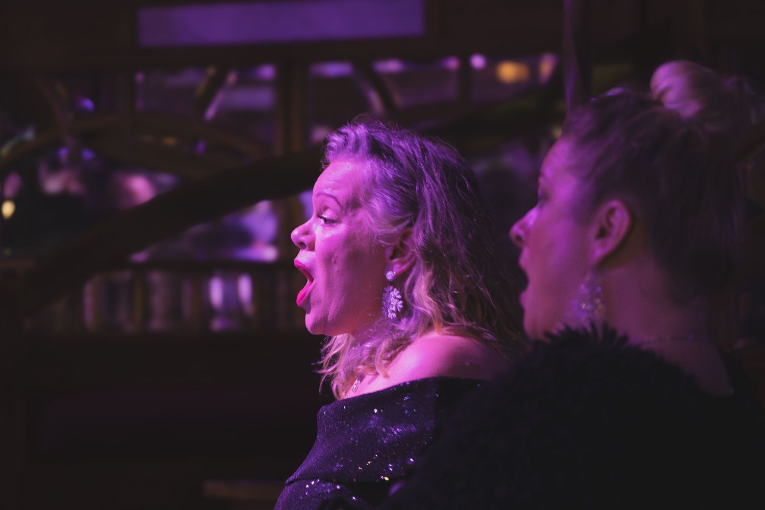 Concert performers in black clothing sing under purple stage lighting.
