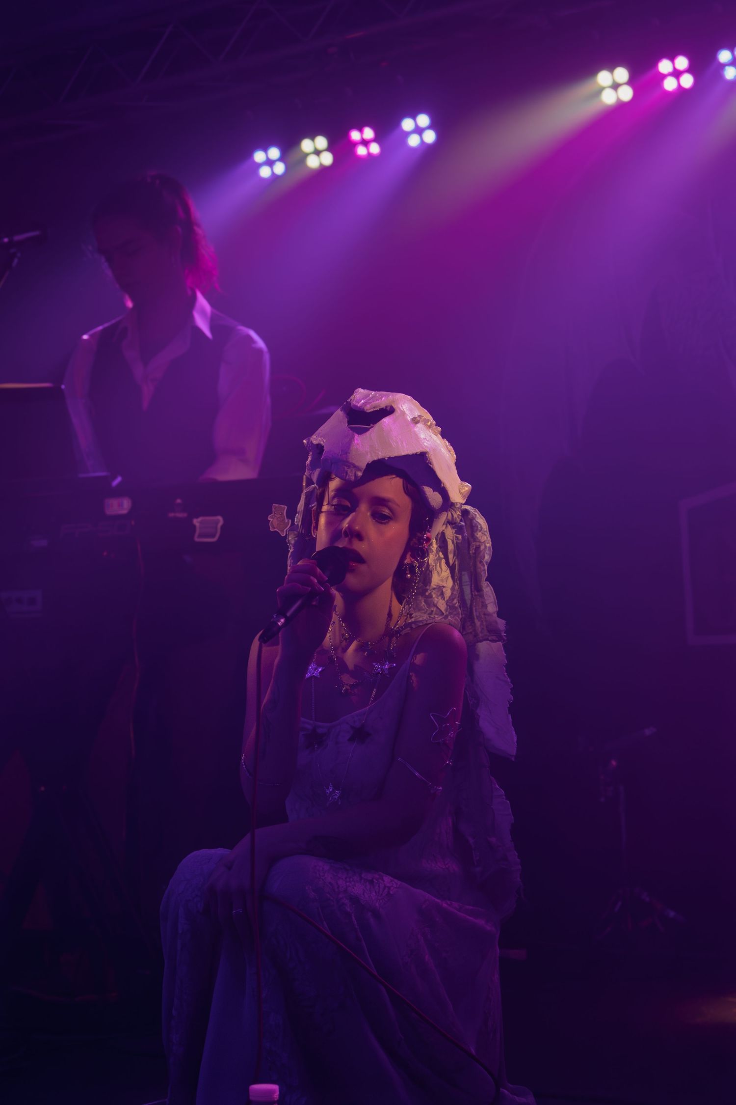 Performer in dramatic lighting sings passionately on stage with purple spotlights creating a moody atmosphere.