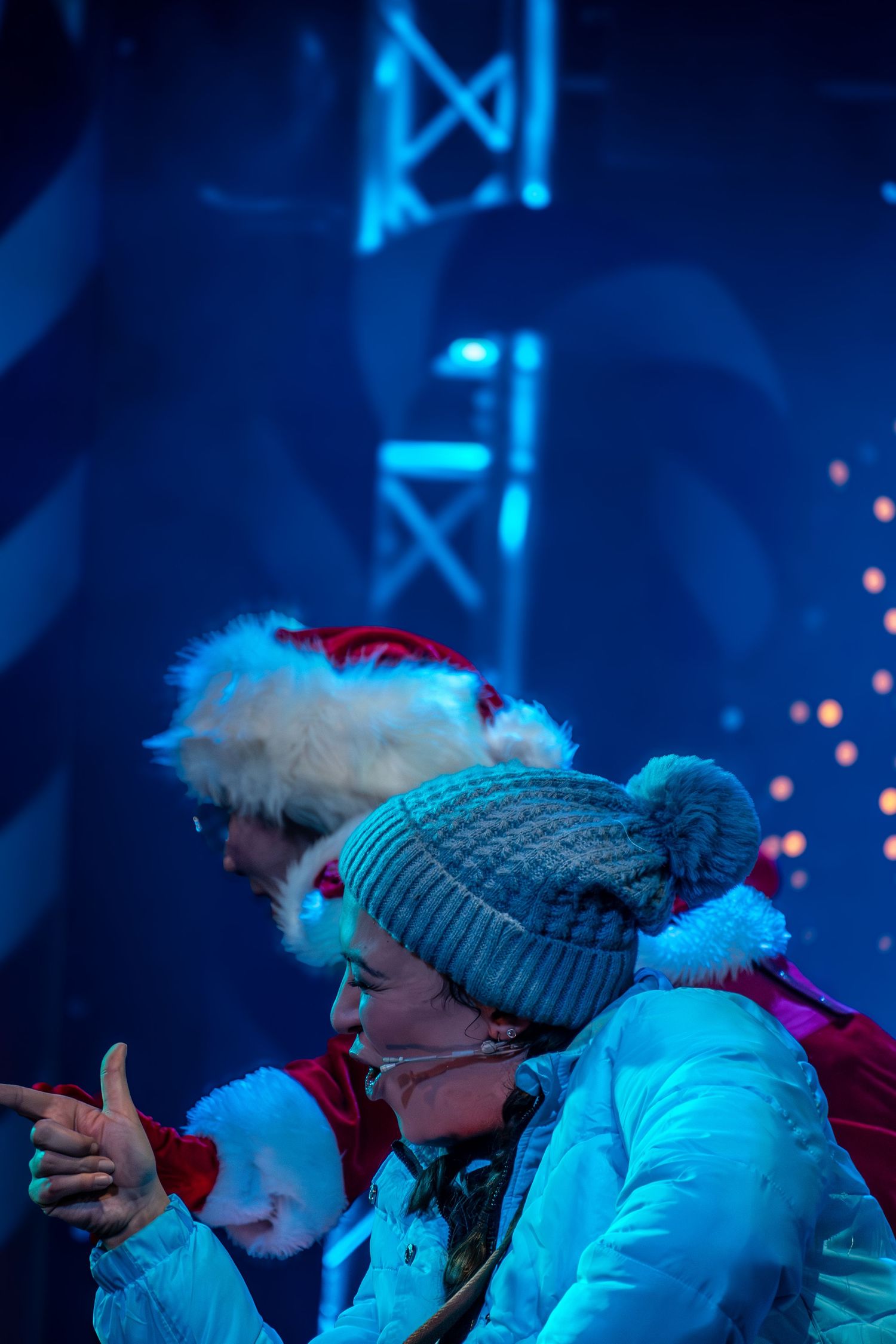 Performers in winter hats and white costumes crouch on stage under blue lighting.