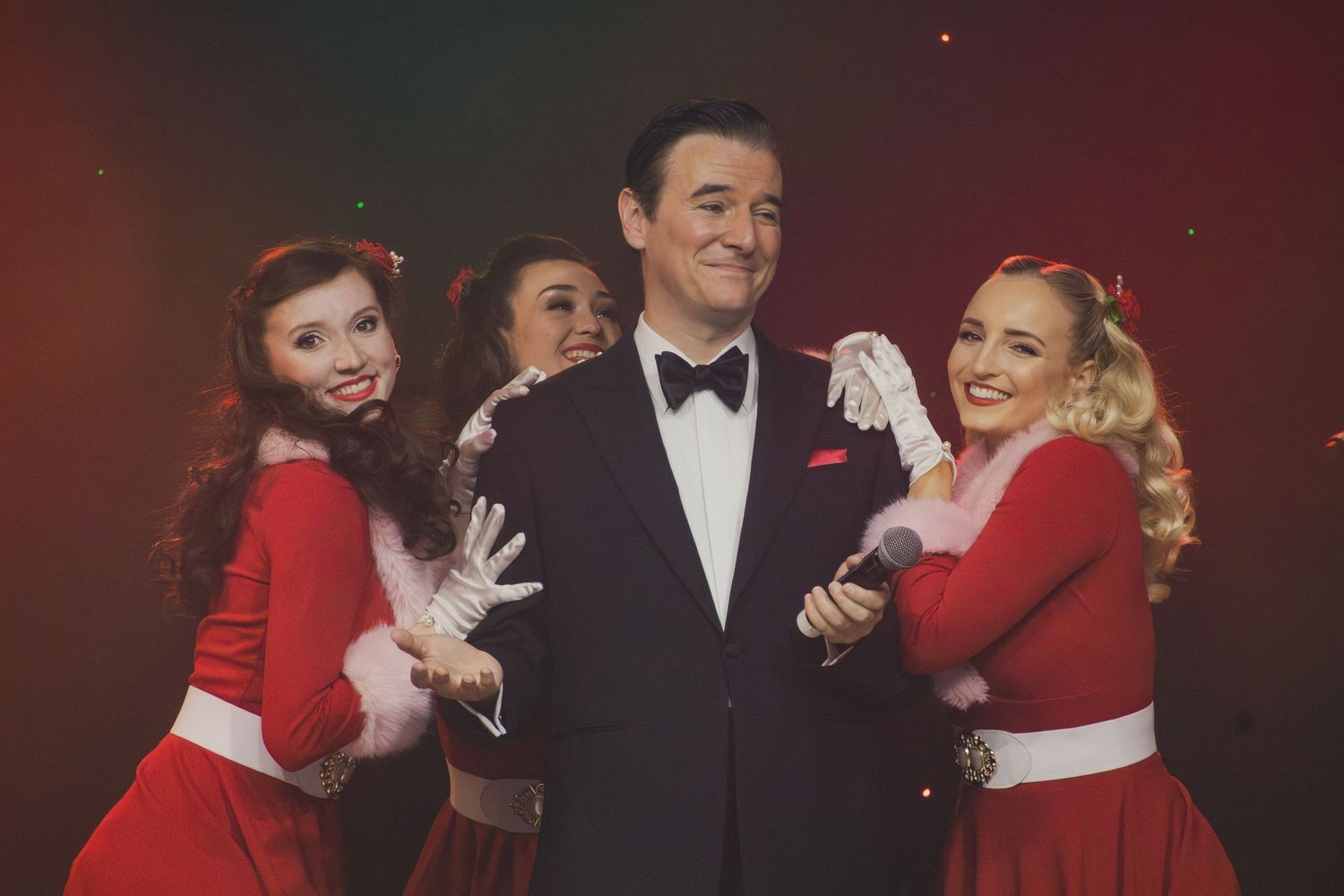 A group of performers in formal attire pose together during a stage show.