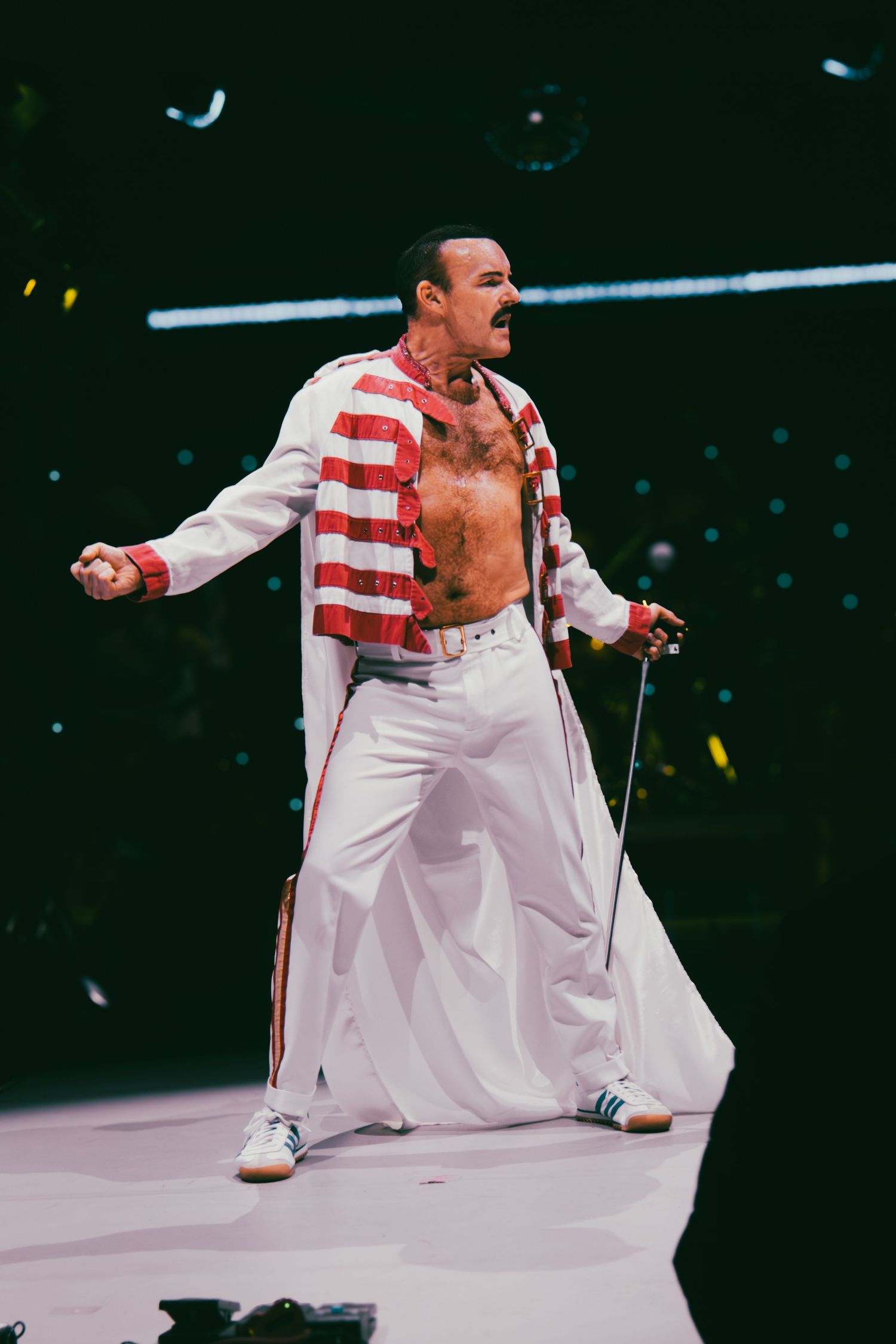 Performer in white and red striped costume crouching dramatically on illuminated stage.