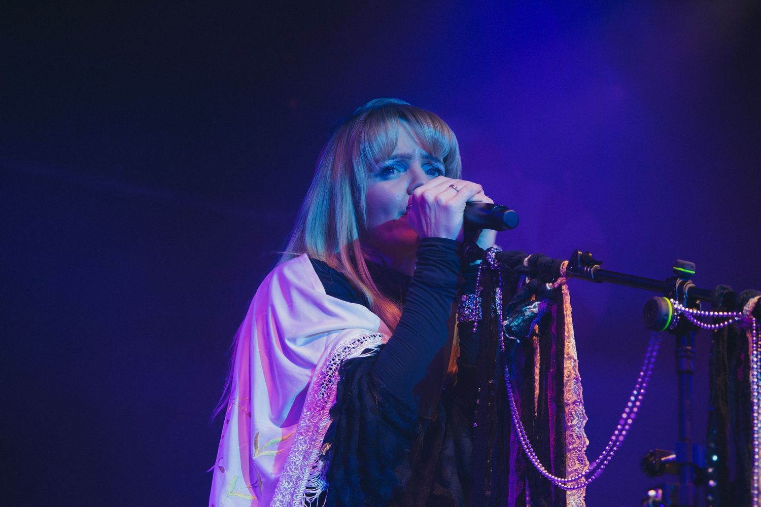 Singer performs on stage with decorated microphone stand under blue concert lighting.