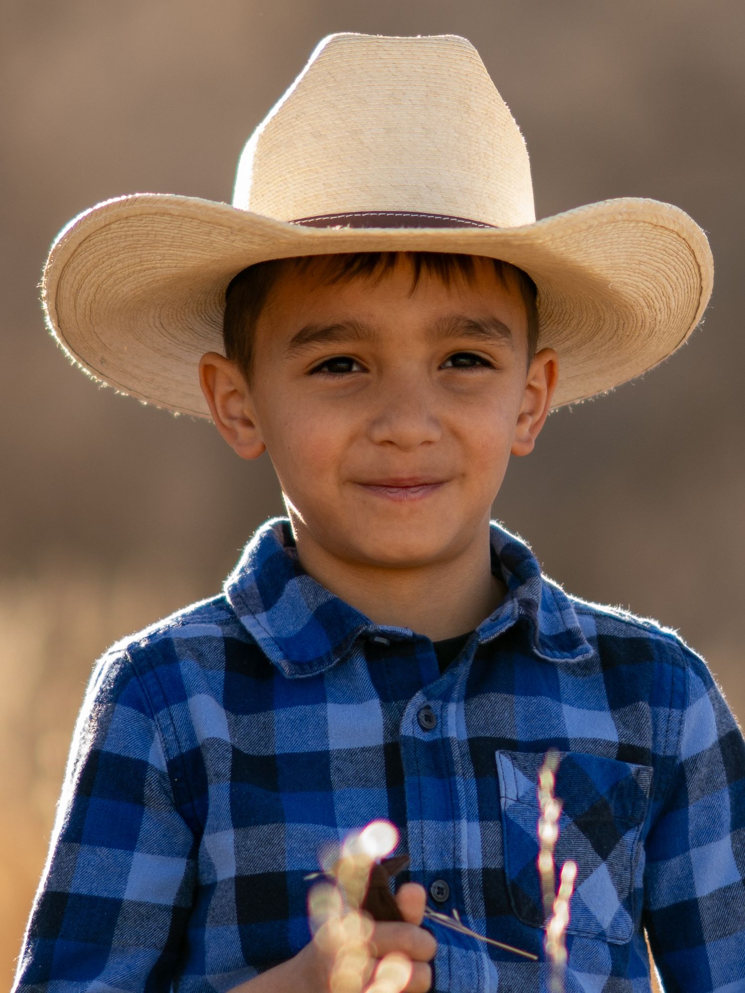 Young child in blue plaid shirt and cowboy hat smiling at camera.