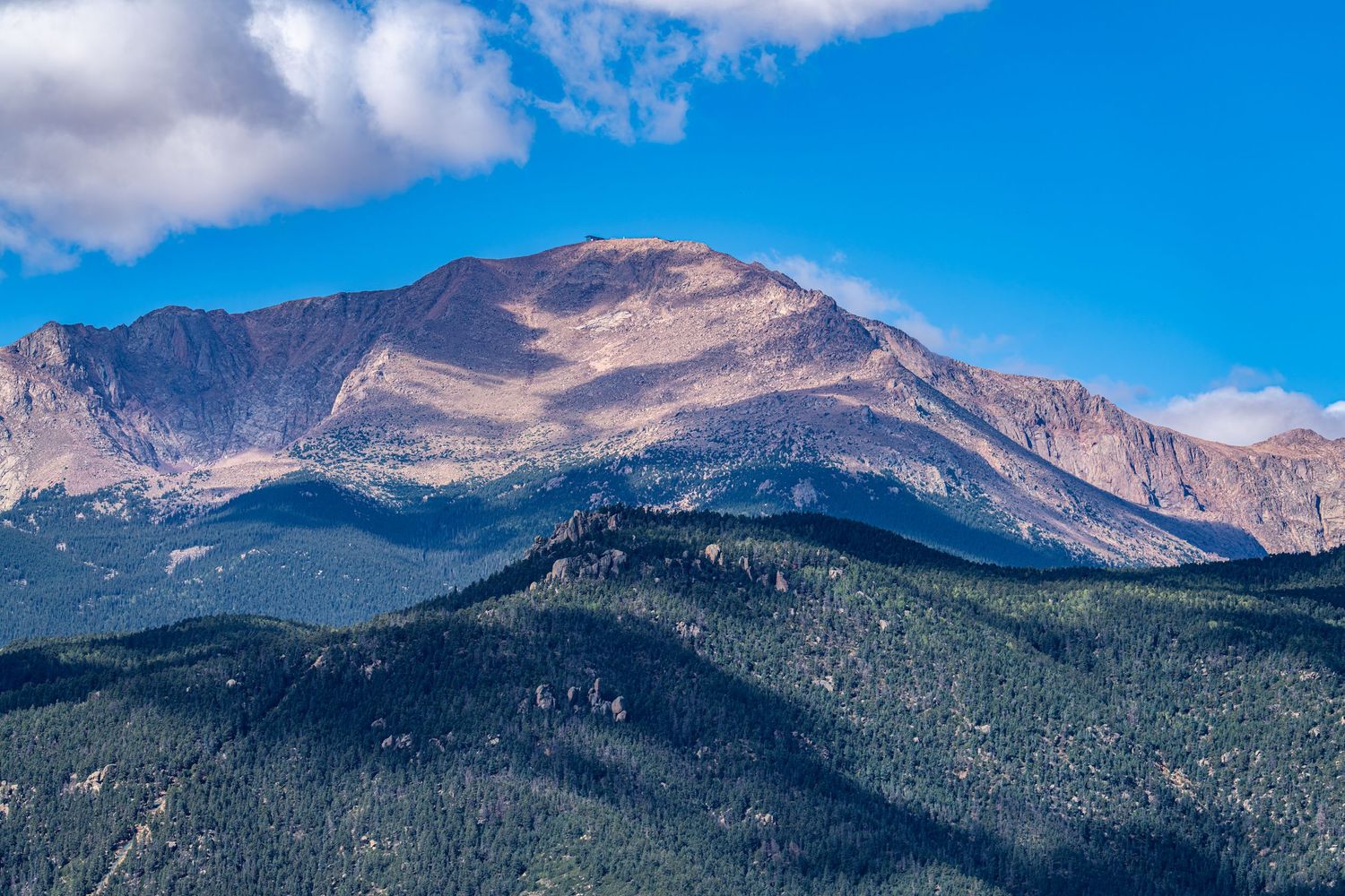 Majestic mountain peaks with rugged terrain under bright blue sky and white clouds.