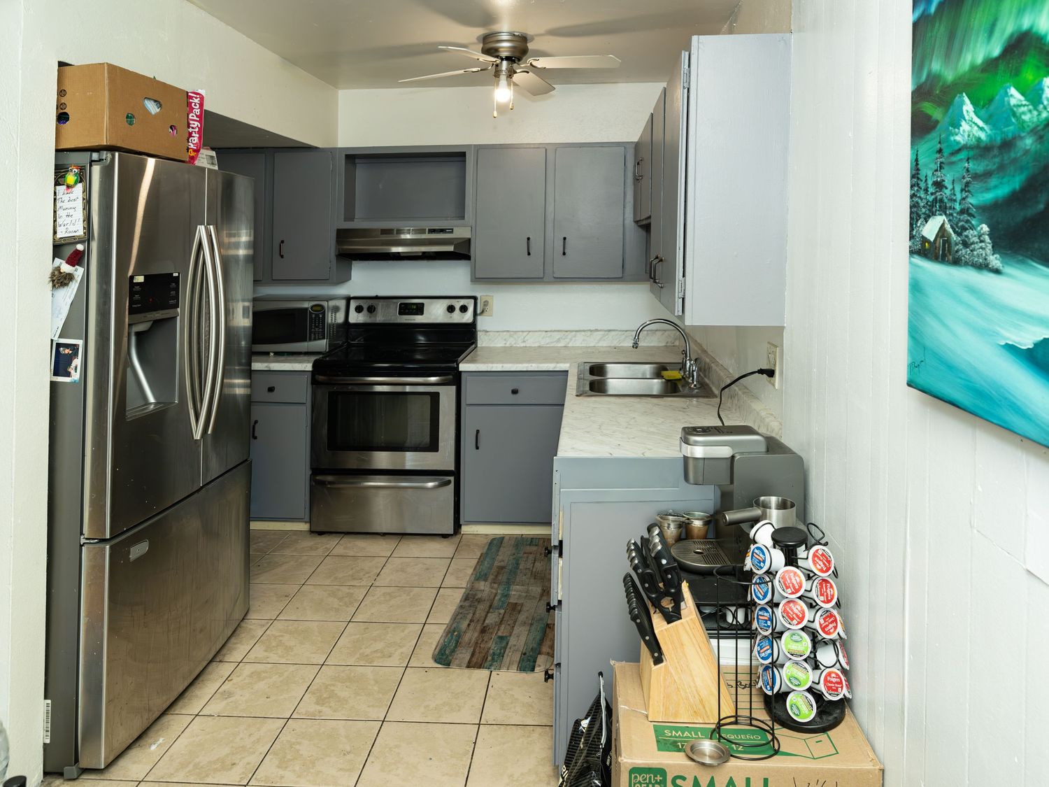 Modern kitchen with stainless steel appliances, grey cabinets, and tile flooring.