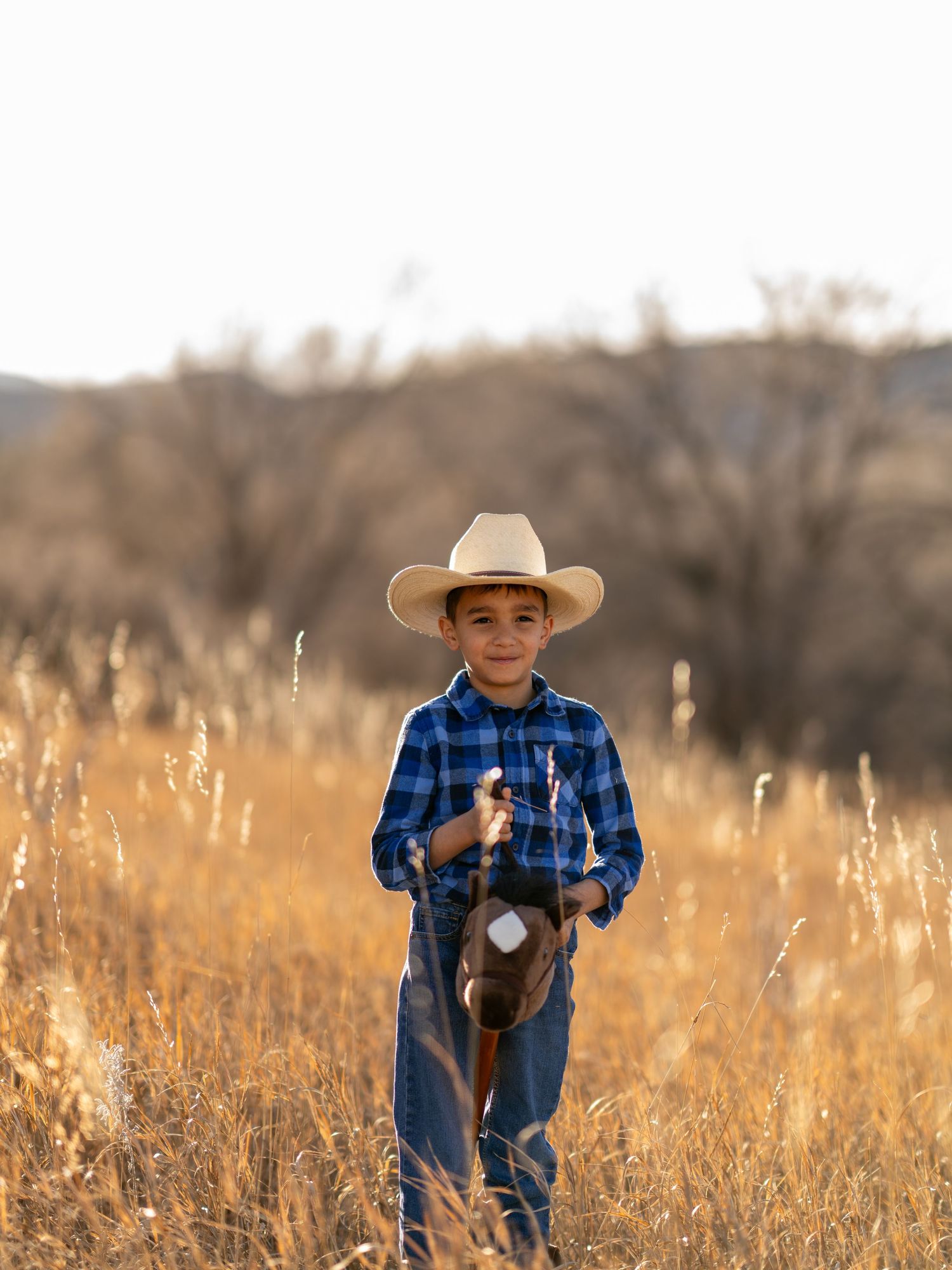 Child in western wear walking through golden grass field at sunset.