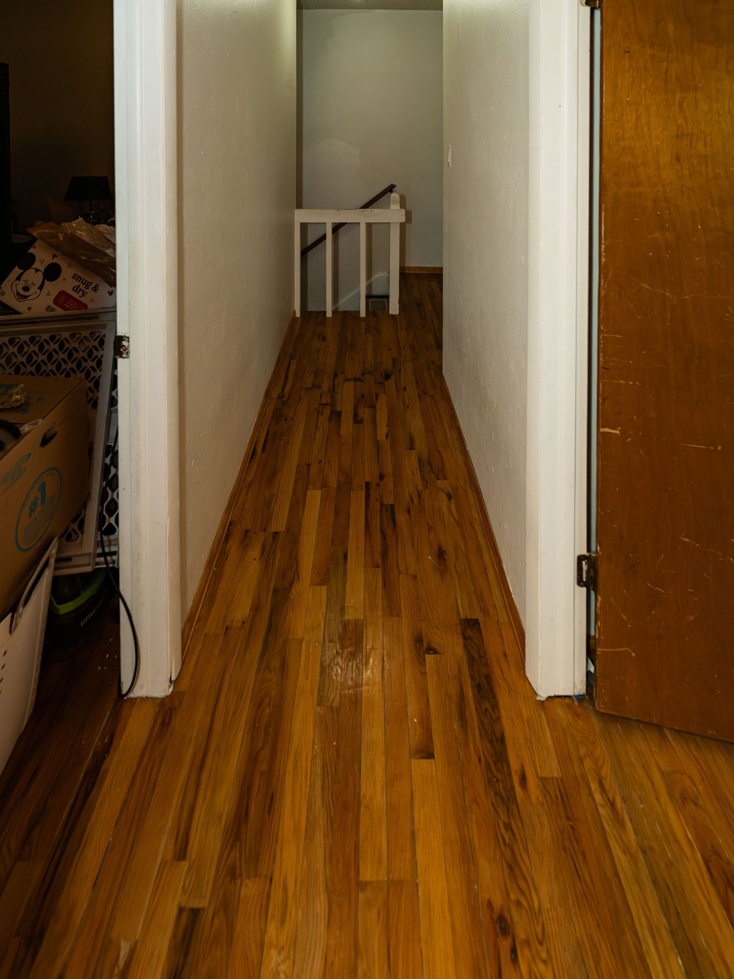 Hallway with polished hardwood flooring and white walls showing natural wood grain.