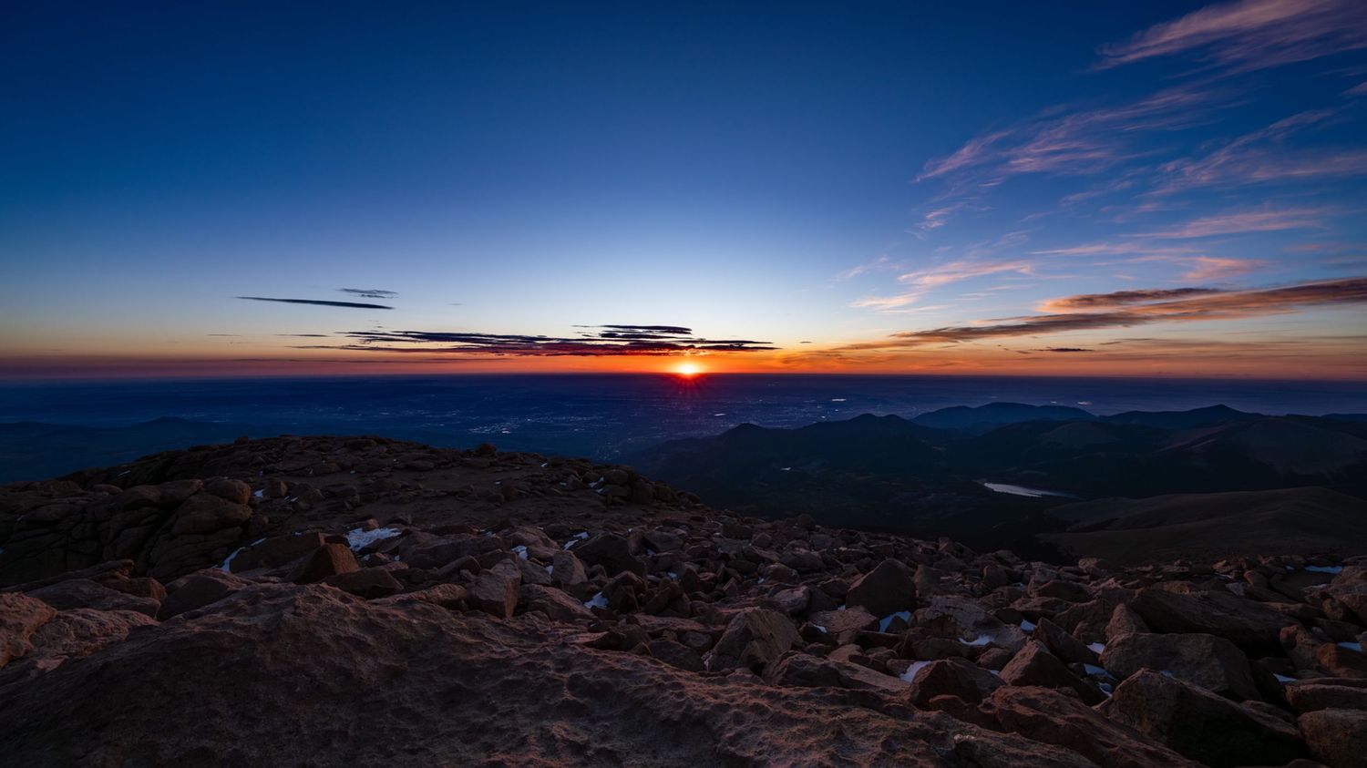 Panoramic mountain landscape at sunset with dramatic blue and orange sky.