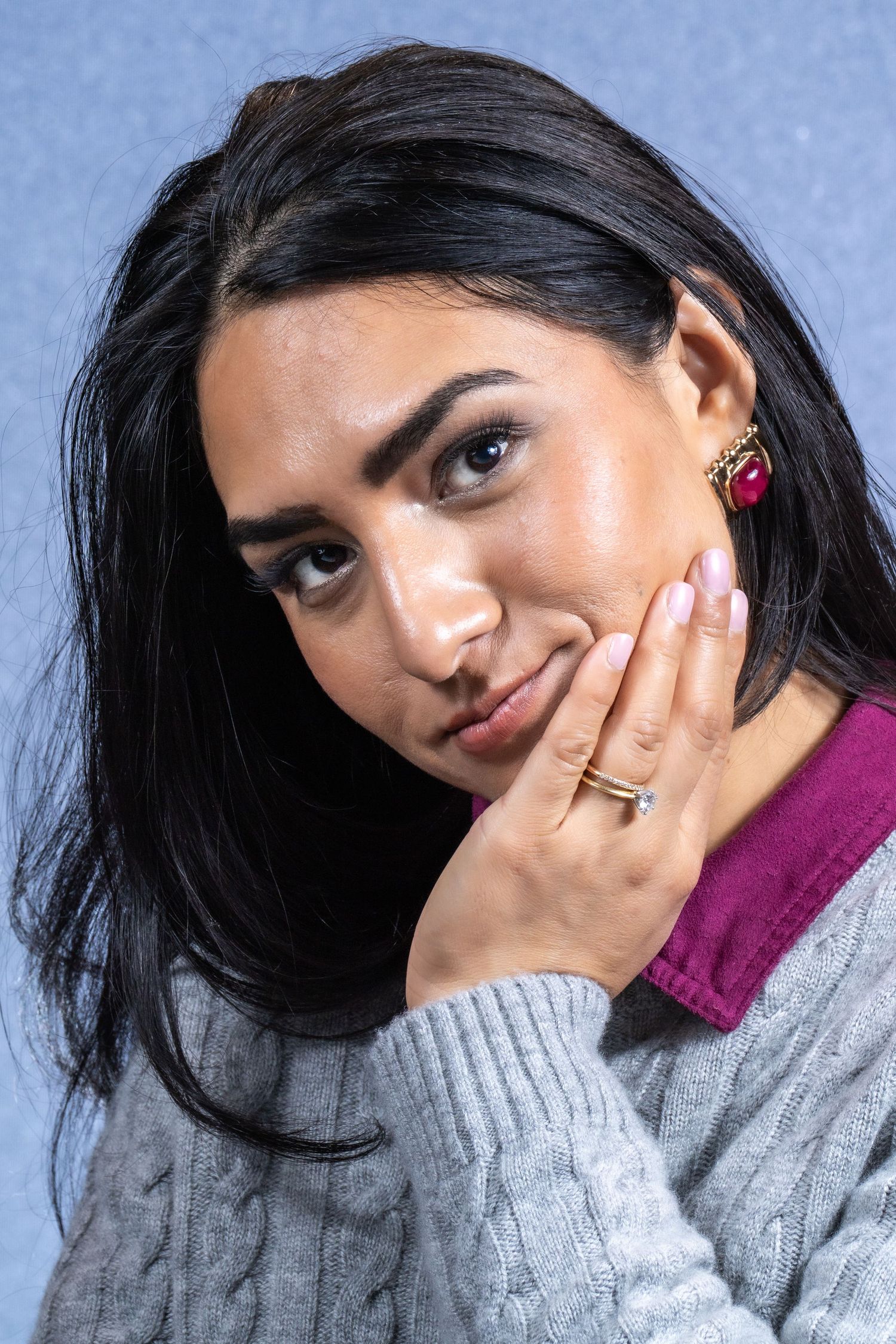 Woman in grey sweater poses playfully against blue background in portrait series.