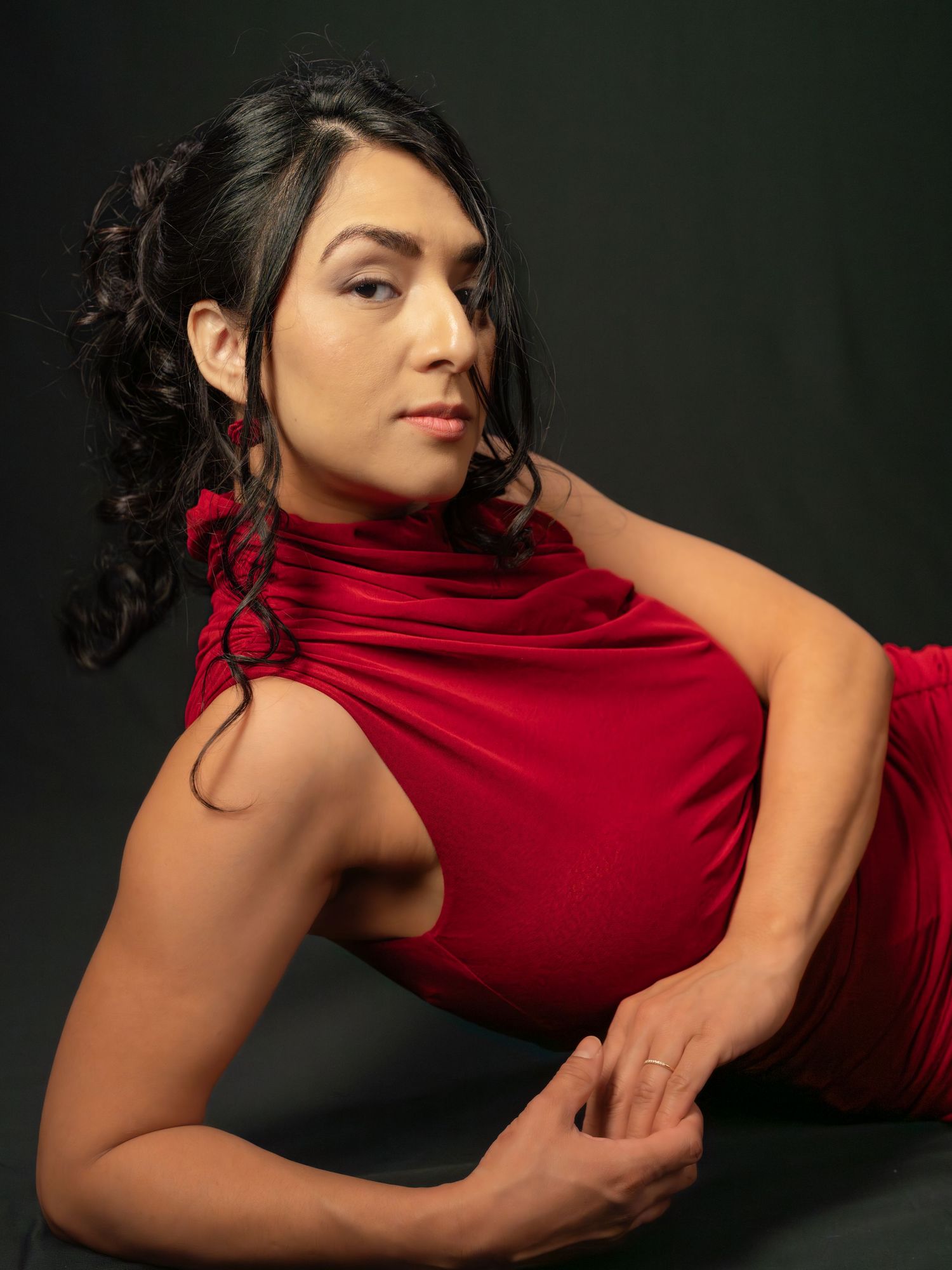 Woman in red dress poses gracefully against dark background in artistic portrait series.