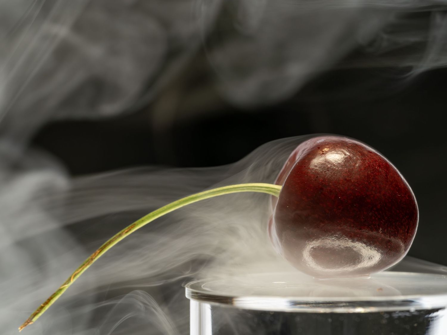 Shiny red apple with water droplets and steam rising against black background.