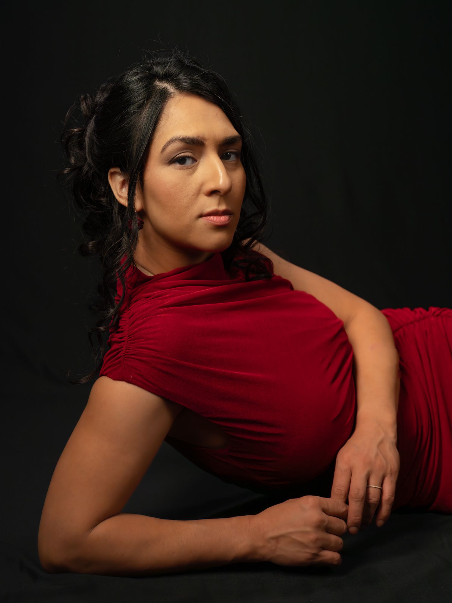Woman in red dress posing elegantly against dark background in professional studio portrait photography.