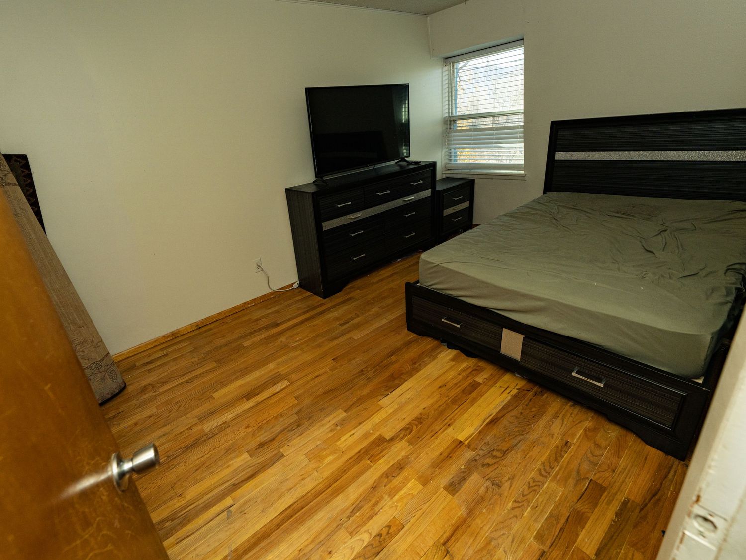 Bedroom with hardwood floors and black furniture against green walls.