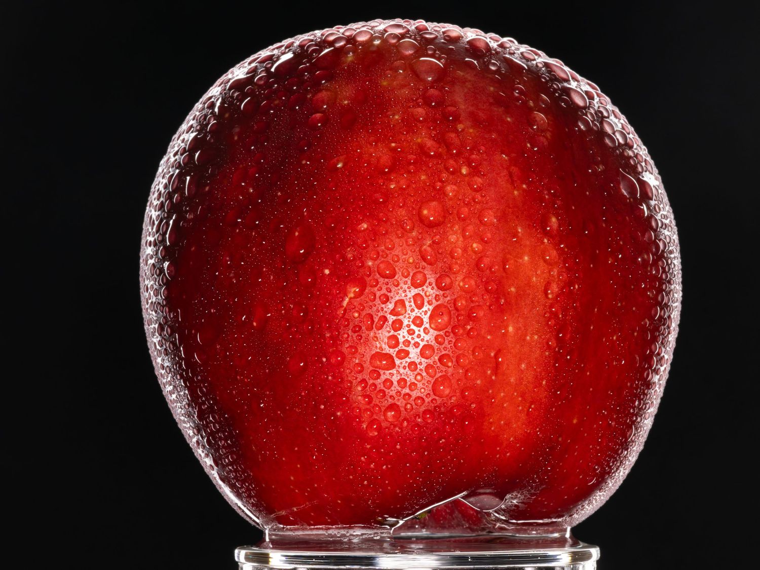 Curved surface of wet red apple showing detailed water droplets and reflective shine.