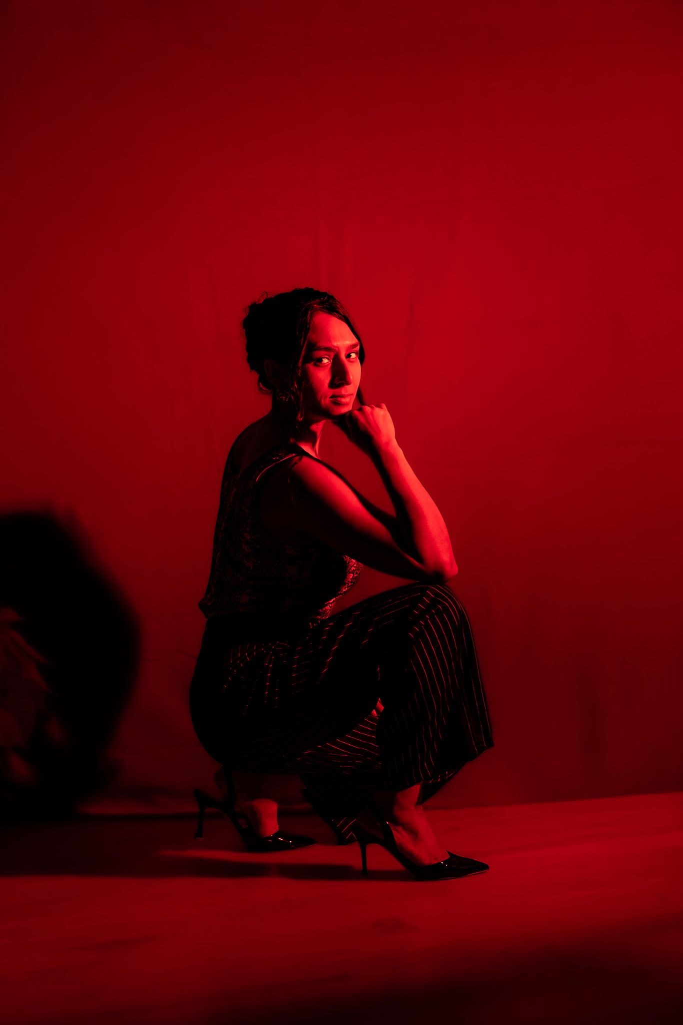 Woman crouching in striped outfit under dramatic red lighting.