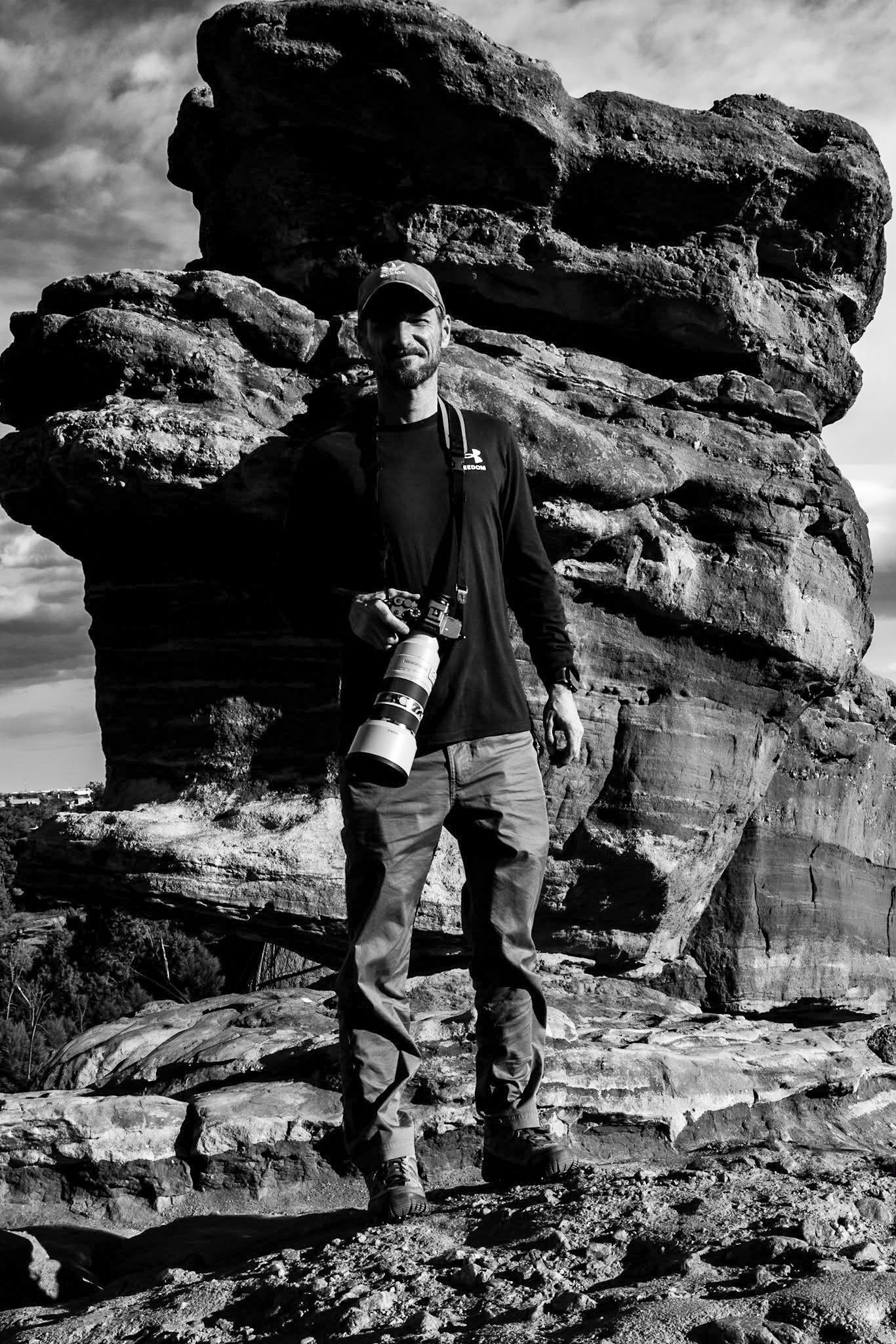 Photographer with professional camera standing by dramatic rock formations in monochrome.
